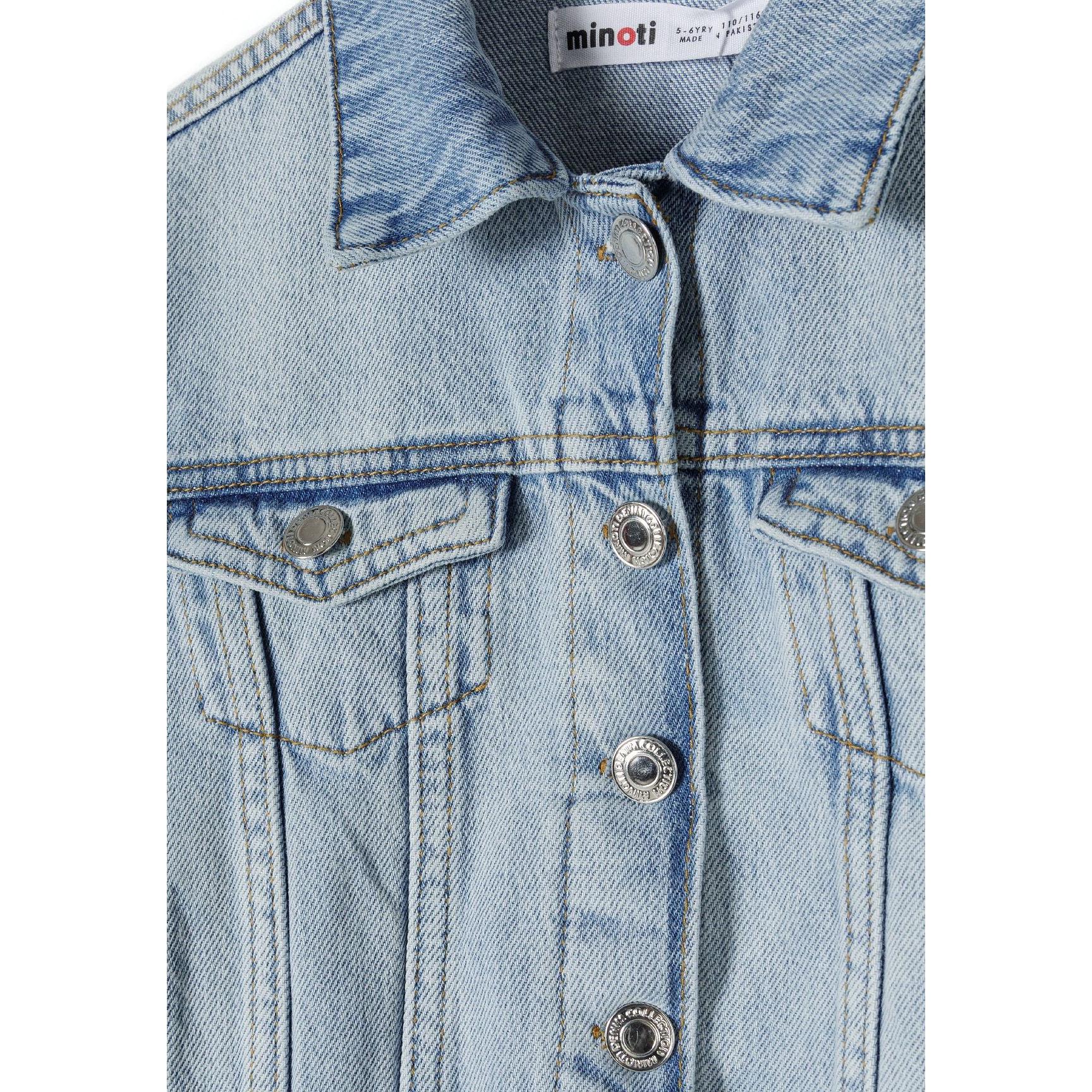 Close-up detail of light blue denim jacket showing Minoti label, chest pockets, and silver-tone button fastenings with classic denim stitching