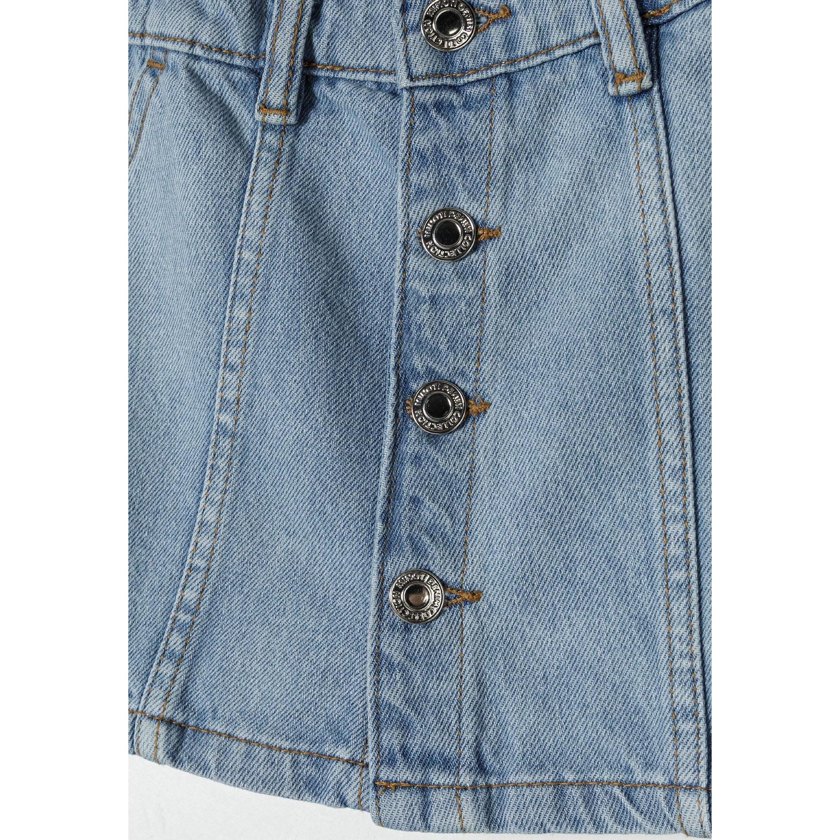 Close-up detail of light blue denim skirt showing metal snap buttons with decorative pattern running down center front with contrast topstitching