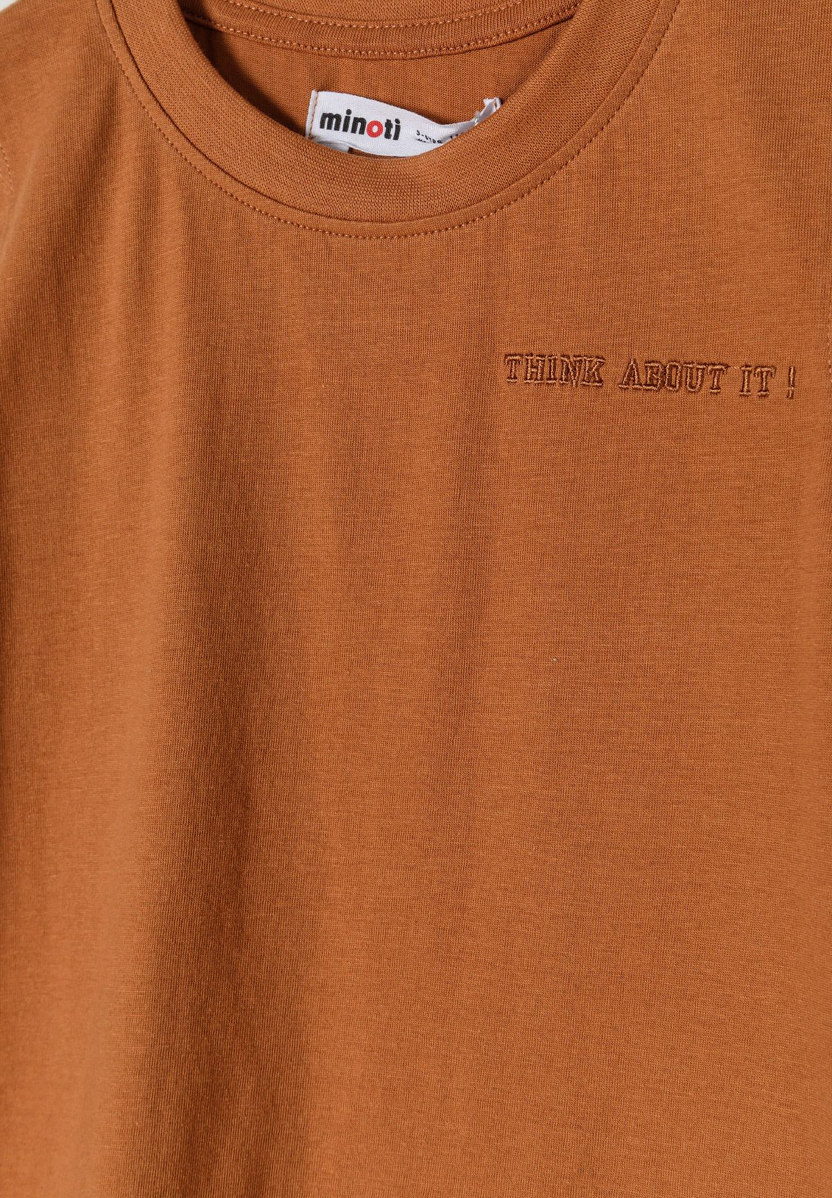 Detail of a boys' beige vest with round neckline and small print.