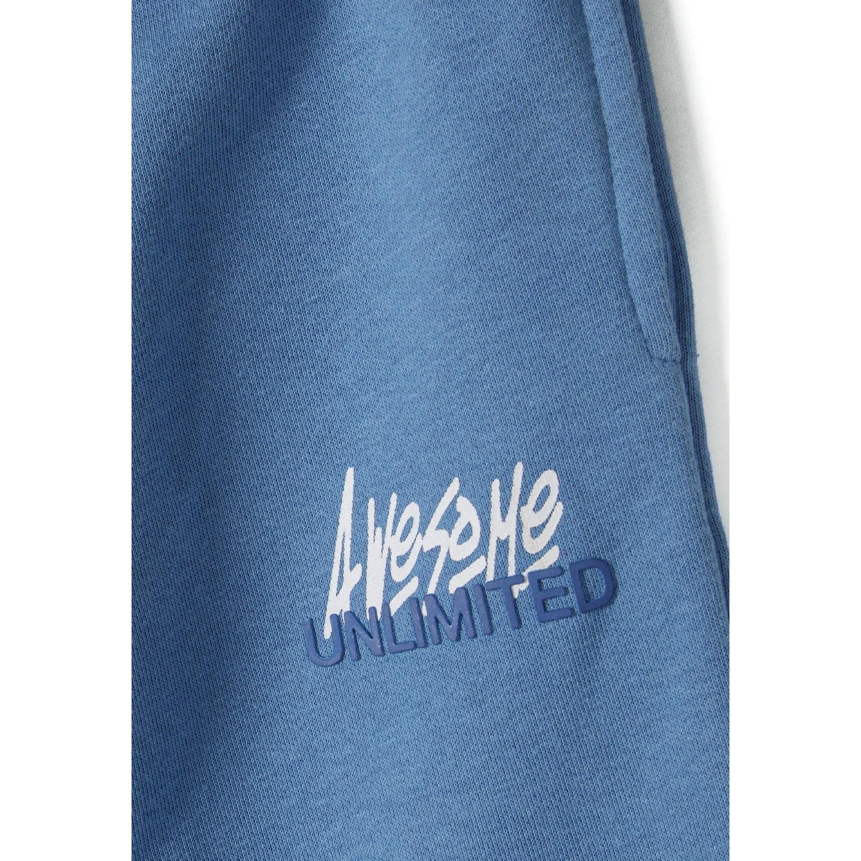 Close-up detail of blue joggers showing white 'Awesome Unlimited' text graphics on the leg