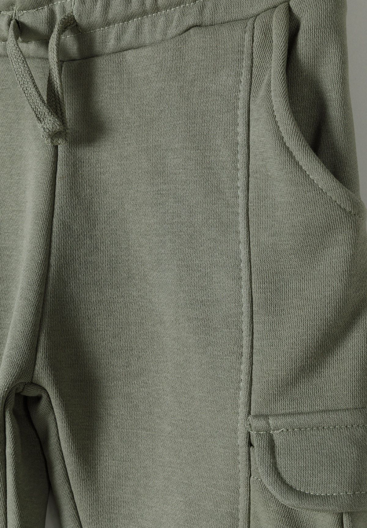 Close-up of olive-green joggers' drawstring waistband, curved hip pocket and cargo-pocket flap.