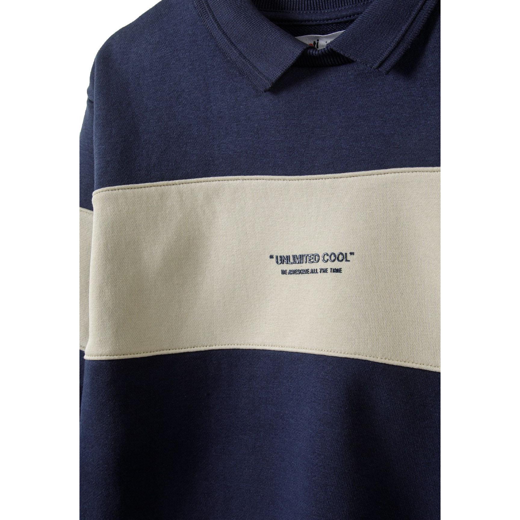 Close-up detail of navy fleece jumper showing polo collar and 'Unlimited Cool' embroidered text on cream chest panel
