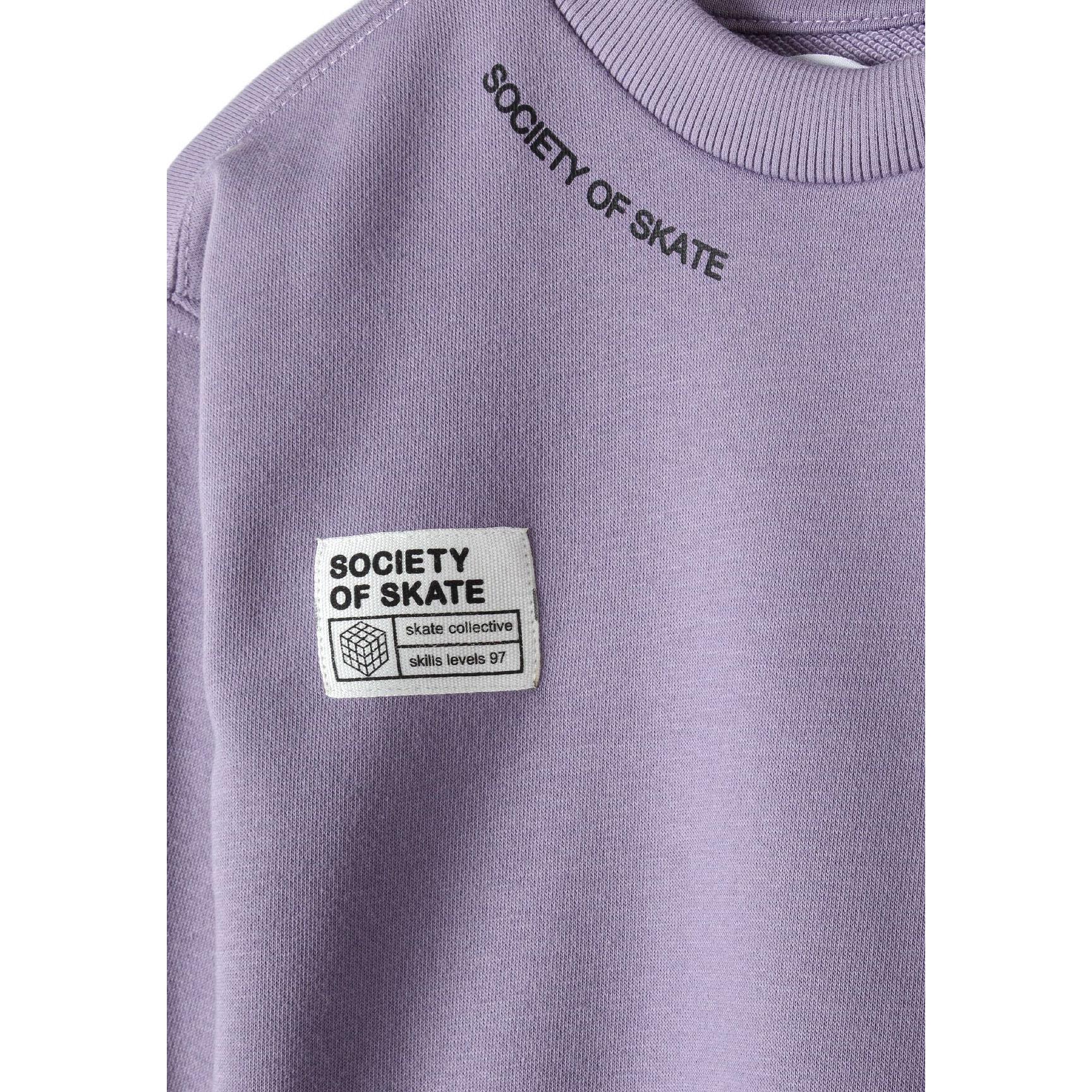 Close-up detail of lilac sweatshirt showing 'Society of Skate' text and white patch with logo on chest