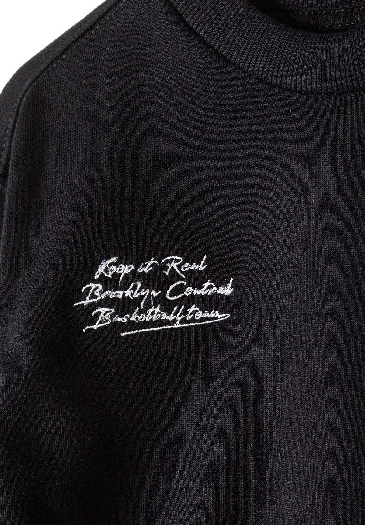 Detail of a black boys' sweatshirt featuring a graphic print and ribbed neckline.