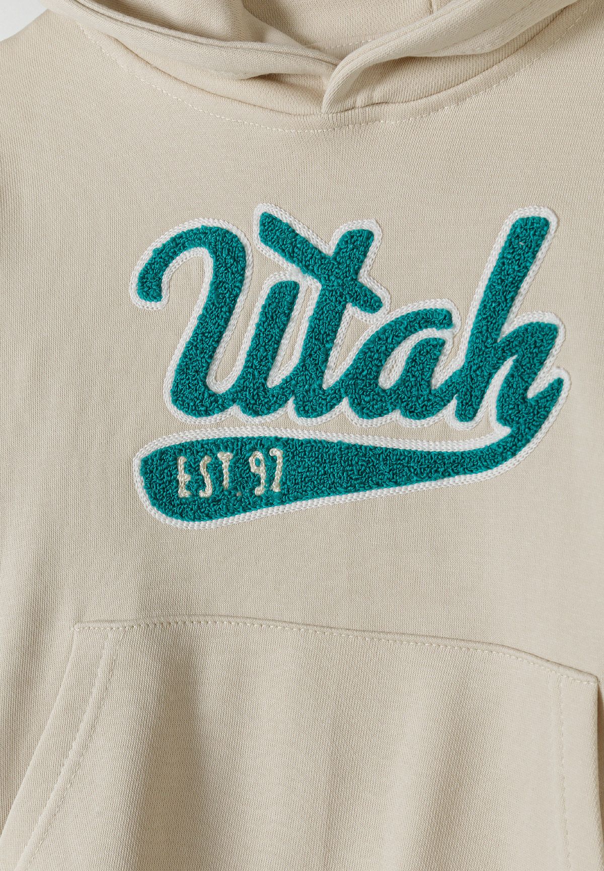 Detail of a cream oversized boys hoodie with kangaroo pocket and decorative print.