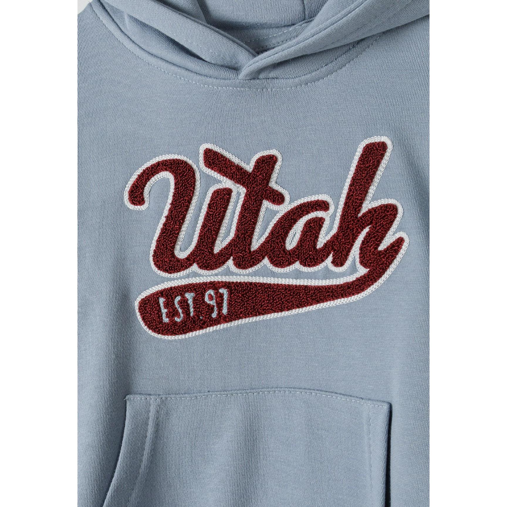 Close-up detail of light blue hoodie showing embroidered 'Utah EST 97' logo in burgundy with white outline and kangaroo pocket