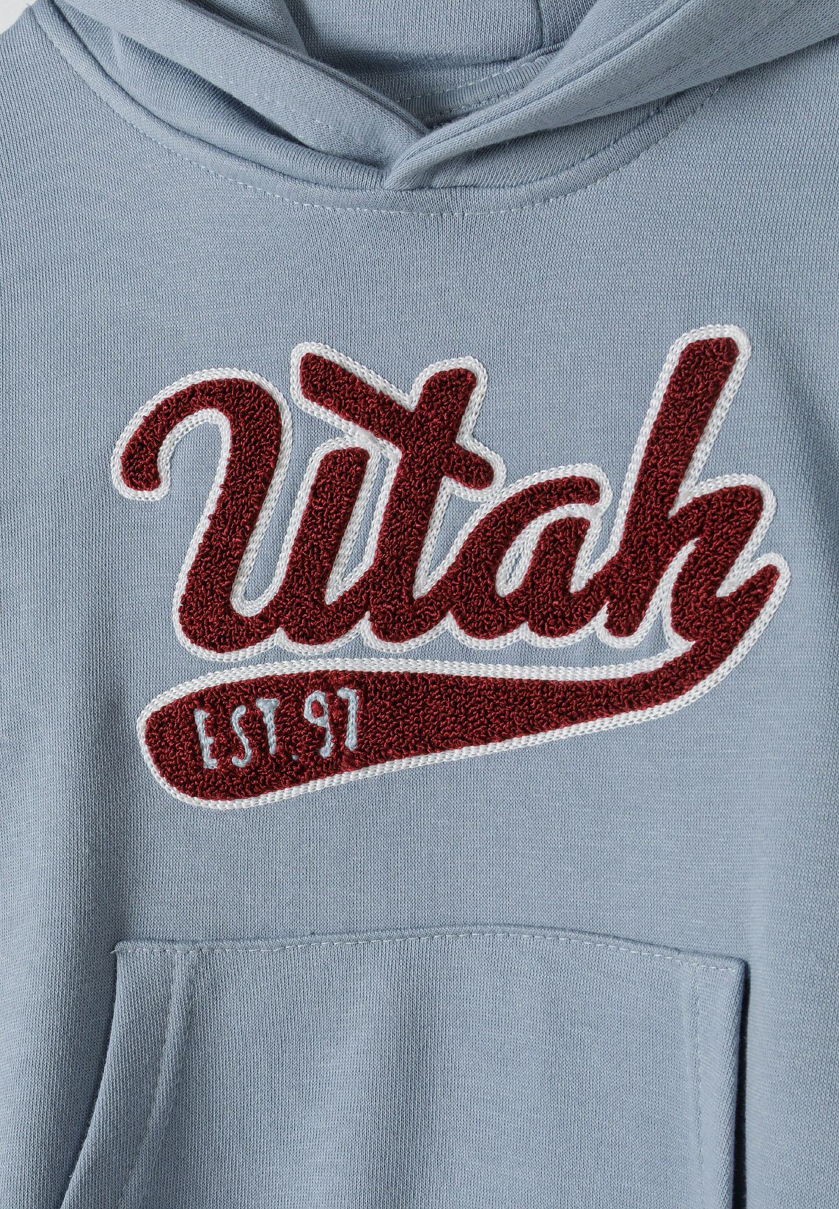 Close-up of textured burgundy Utah EST 97 logo on light blue hoodie.