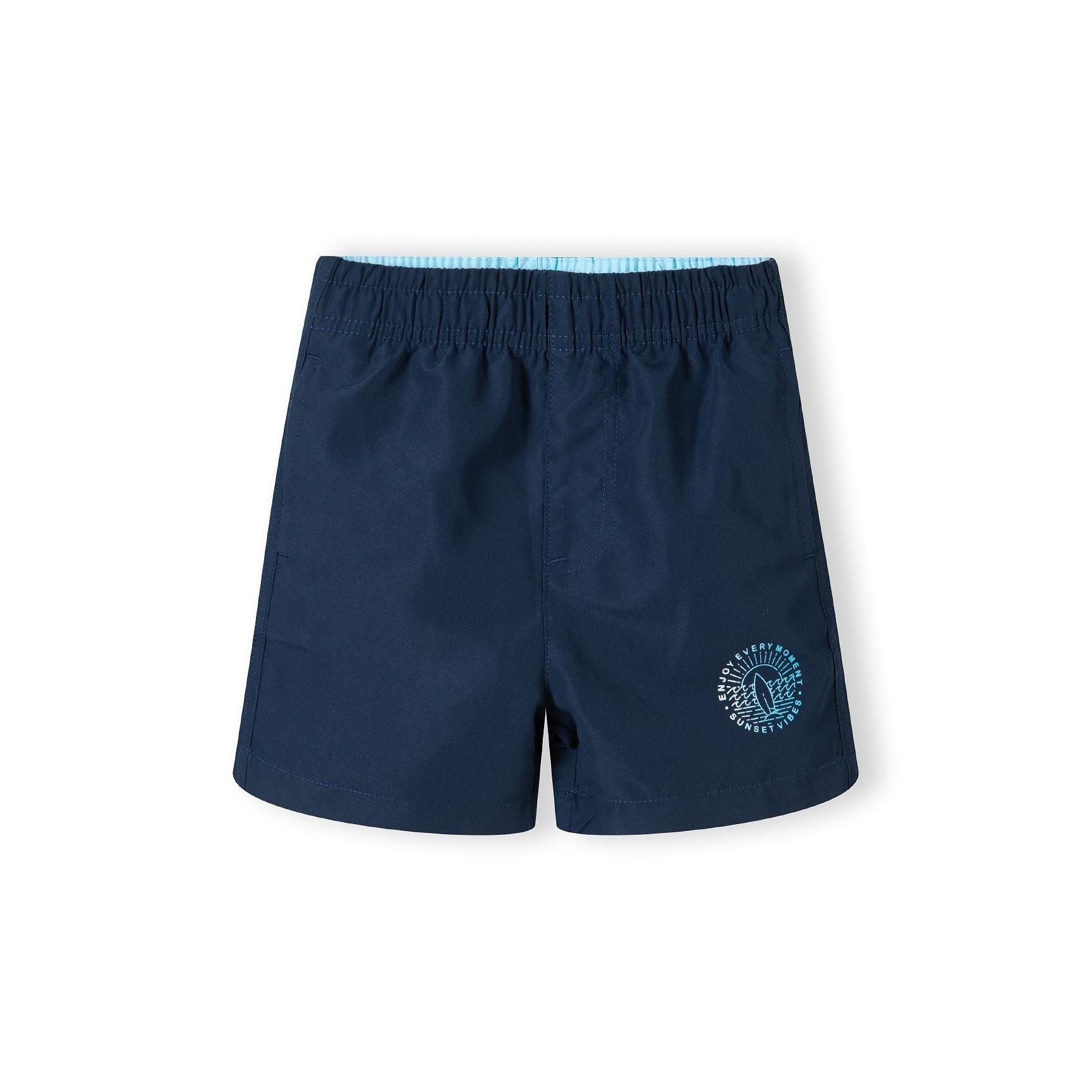 Back view of blue camouflage print swim shorts with elastic waistband showing Minoti brand label on white background