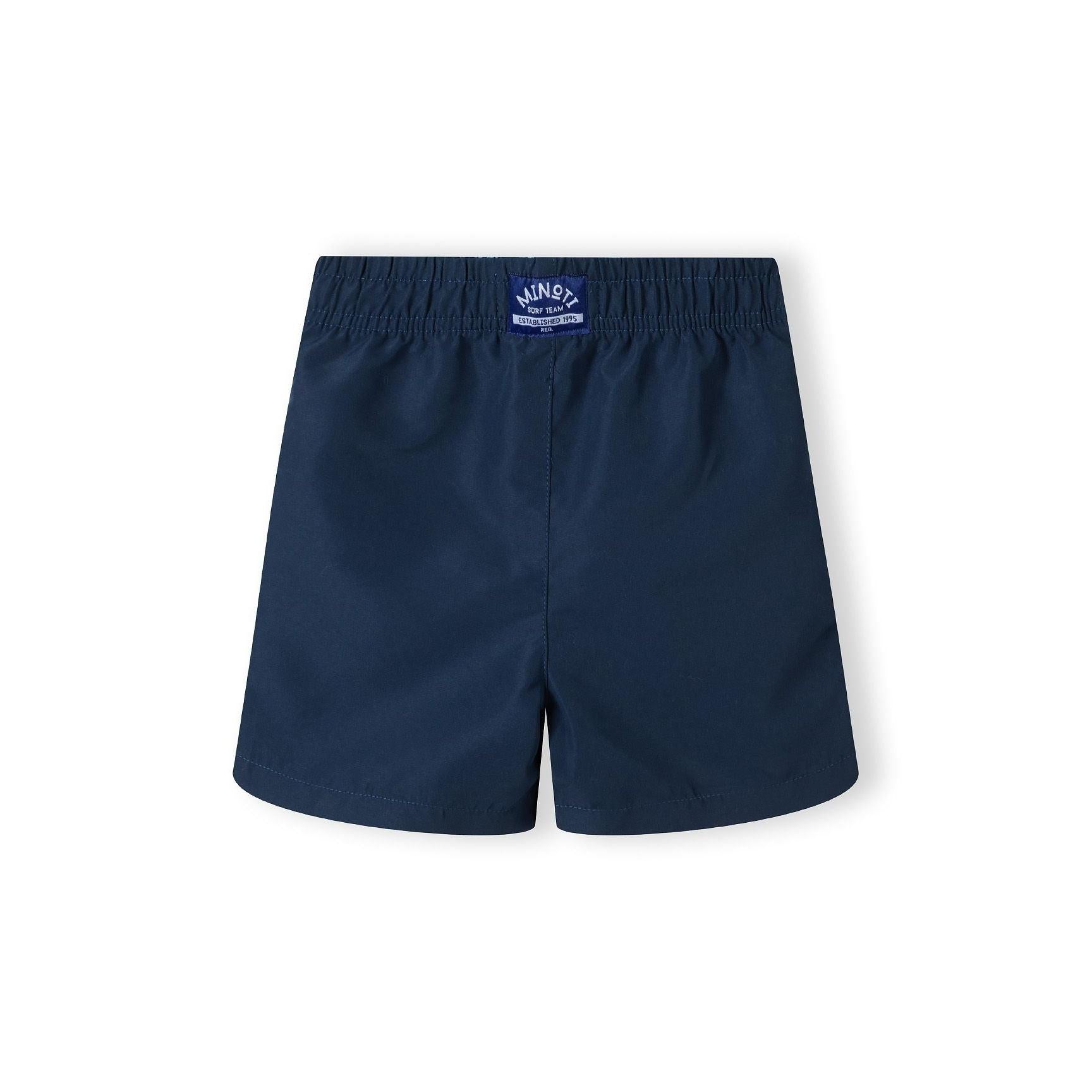 Back view of solid navy swim shorts with elastic waistband showing Minoti brand label on white background
