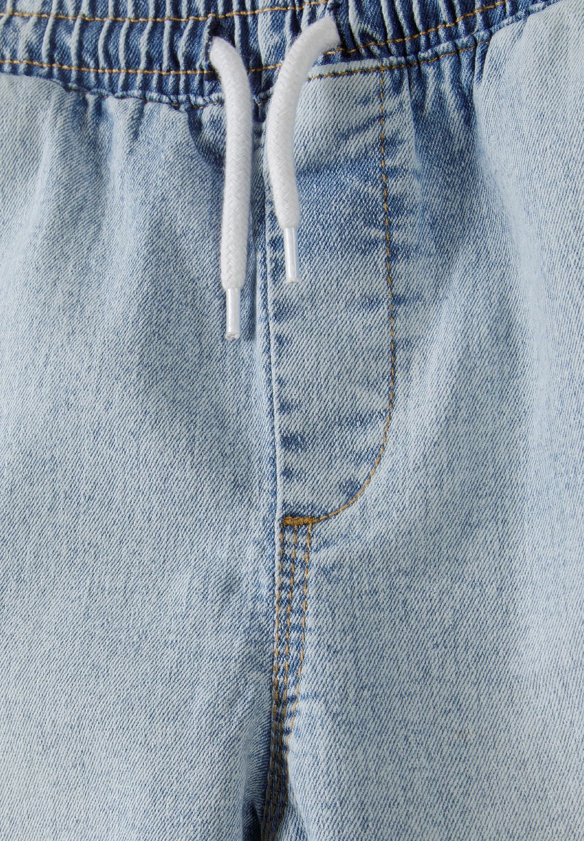 Detail of boys light blue denim cargo shorts with elasticated waistband and drawstrings.
