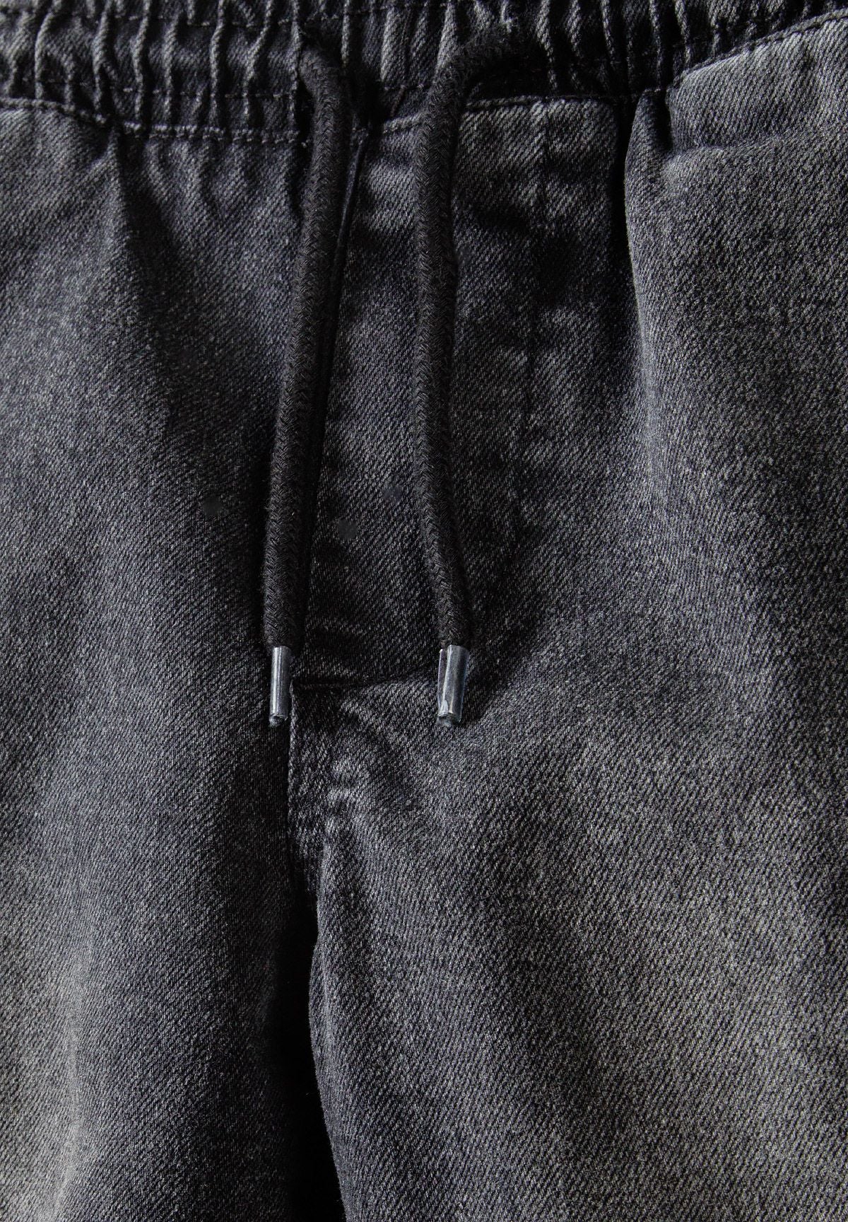 Detail of black denim cargo shorts with drawcord and elasticated waistband.