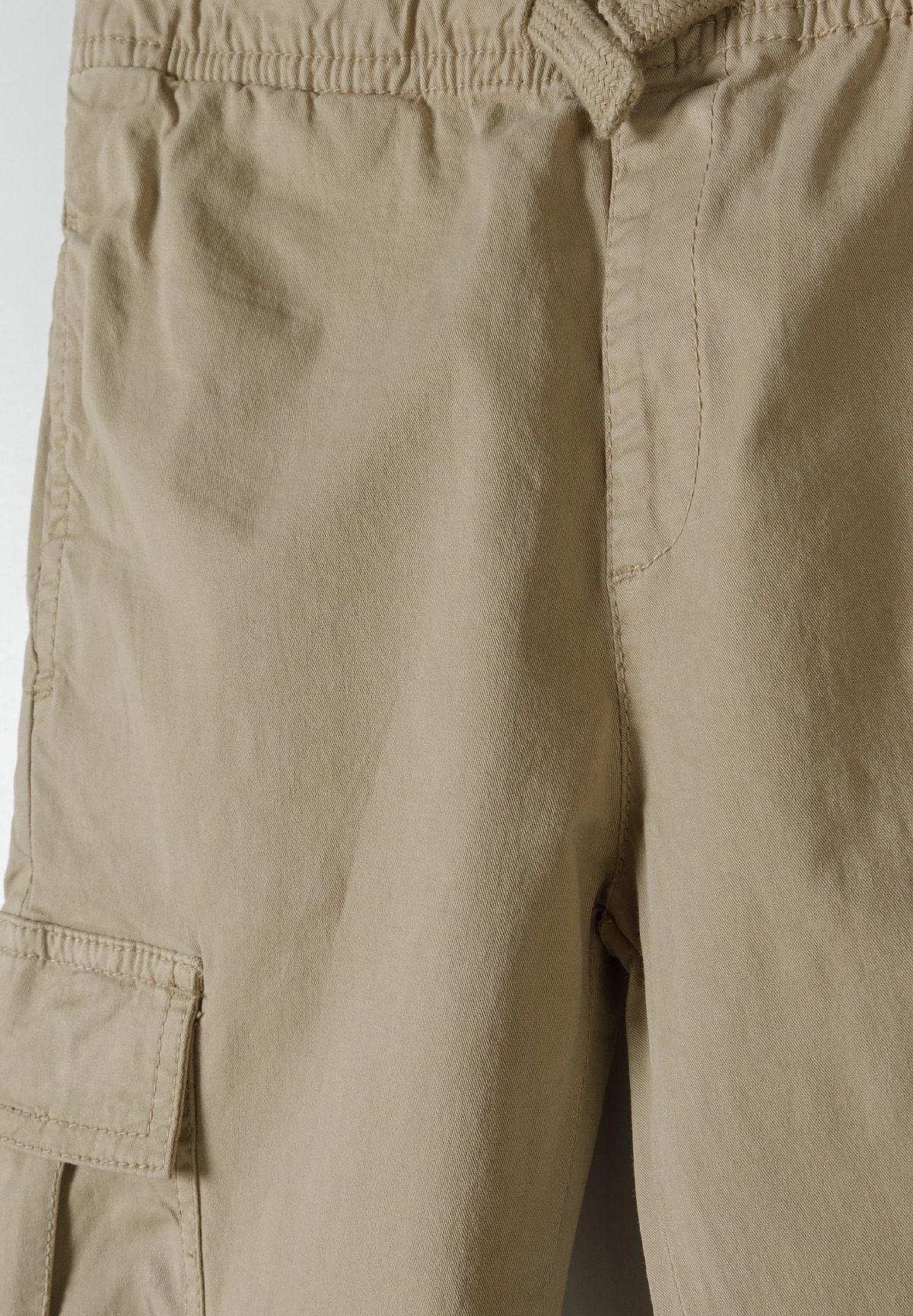Detail of boys' grey woven cargo trousers with elastic waistband and side pockets.