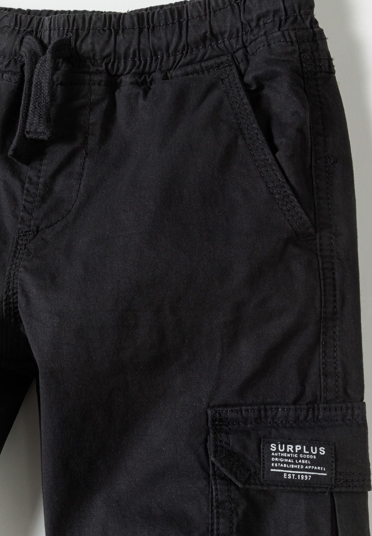 Boys black cargo trousers, close-up view of waistband and pocket.