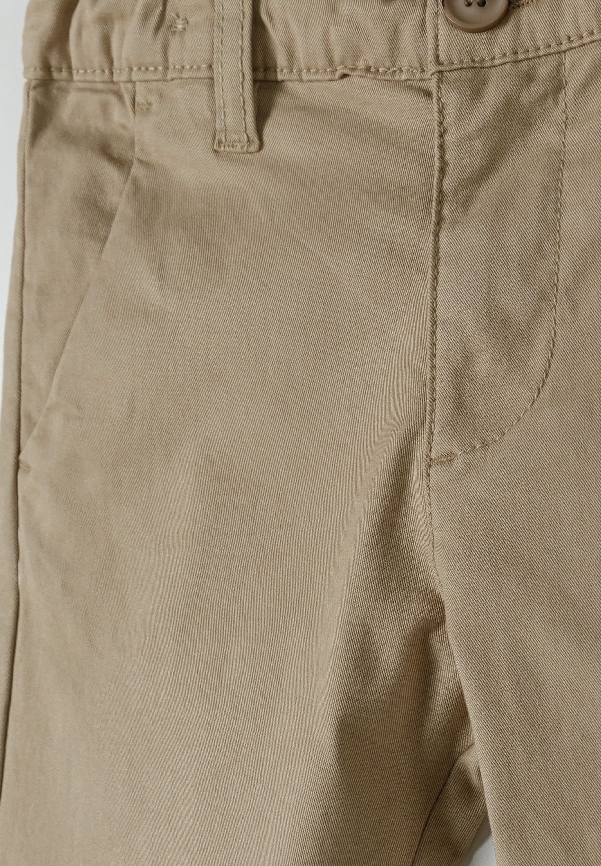 Detail of boys chino trousers with adjustable waistband and button closure in beige.