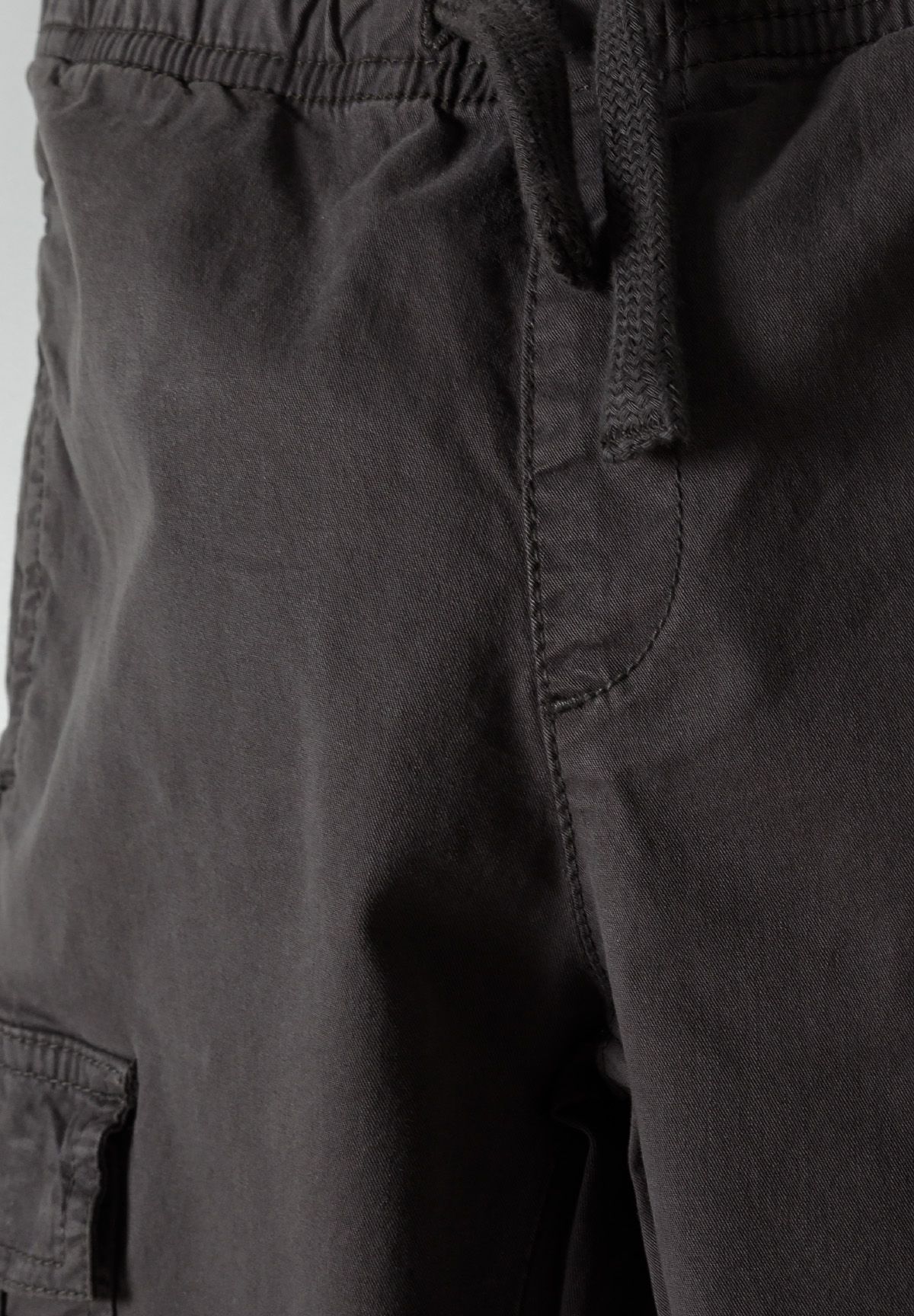 Close-up of boys' grey woven cargo trousers featuring an elastic waistband and side pocket.