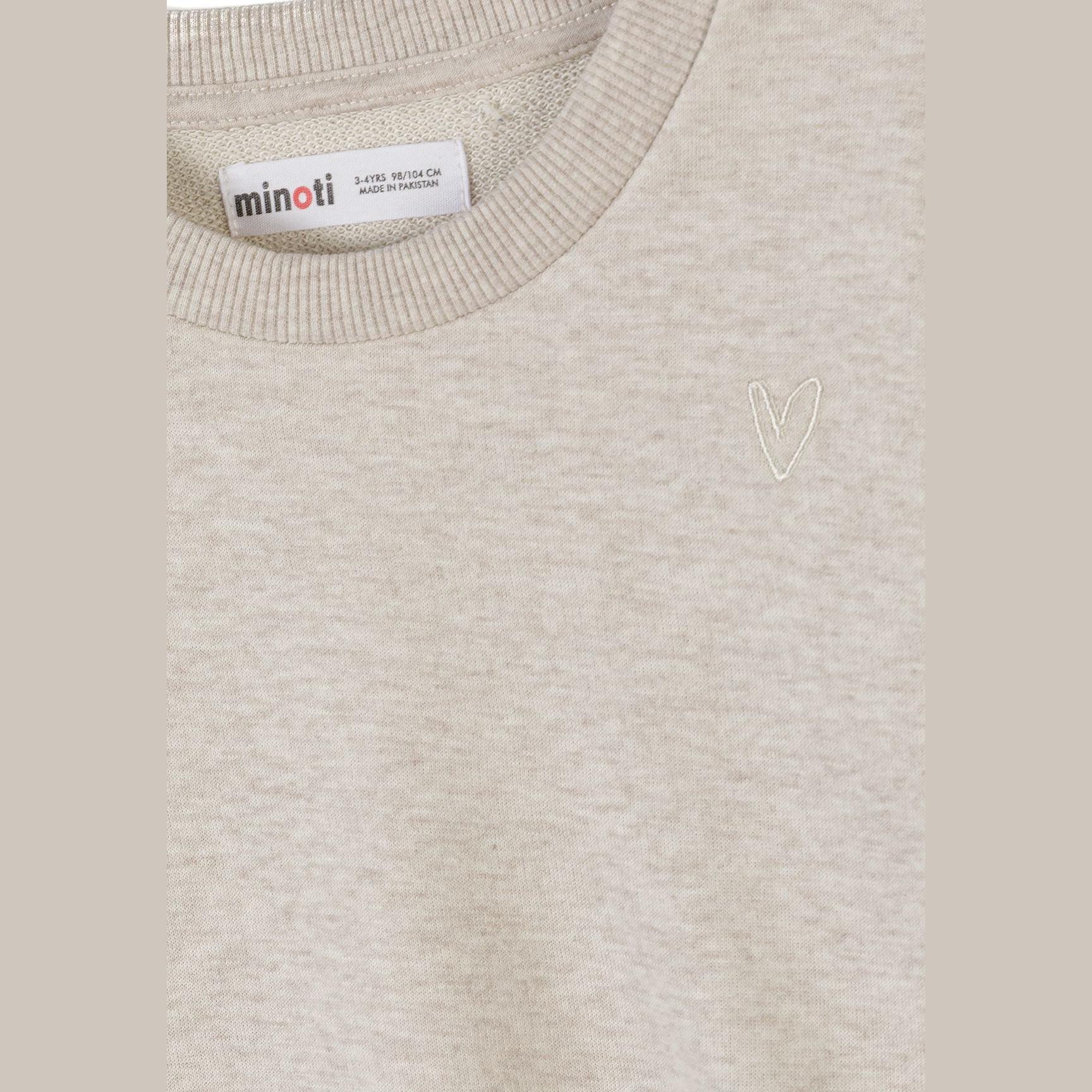 Close-up detail of coral pink sweatshirt showing embroidered white heart motif and ribbed crew neckline