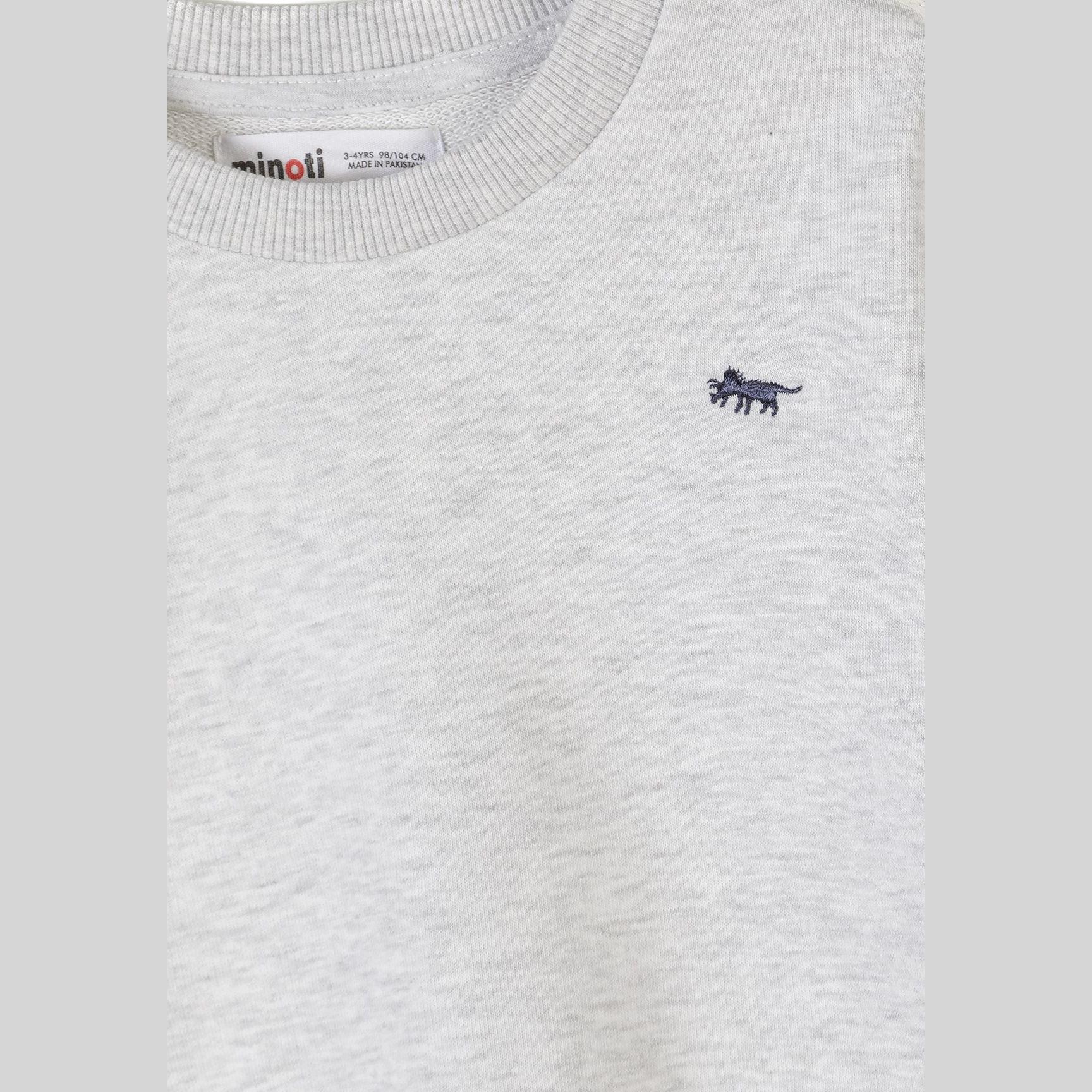 Close-up detail of grey sweatshirt showing Minoti label at neck and small embroidered navy dinosaur logo on chest