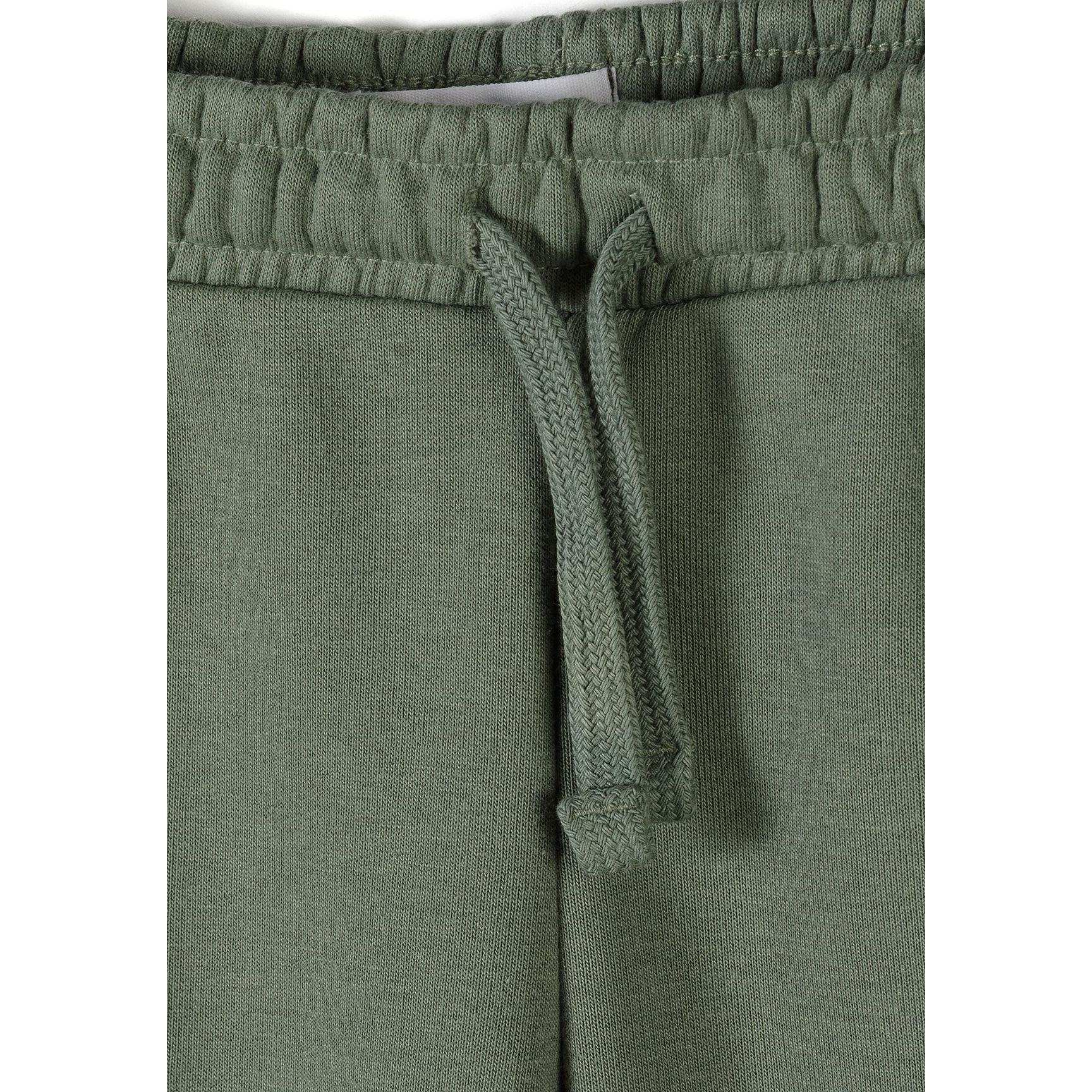 Close-up detail of olive green joggers showing elastic waistband with drawstring ties for comfortable fit