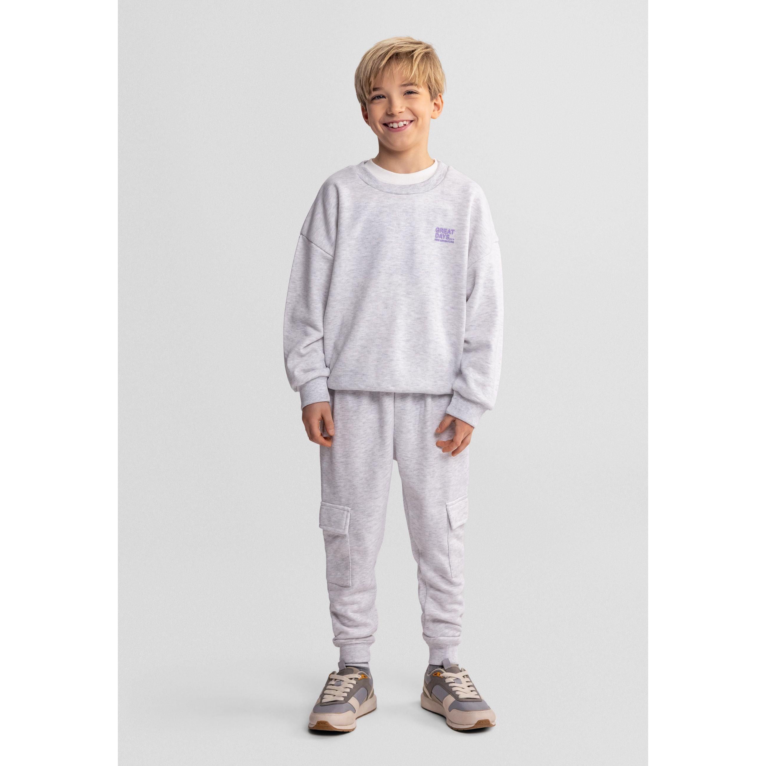 Young boy wearing grey marl sweatshirt with matching joggers, smiling against white studio background
