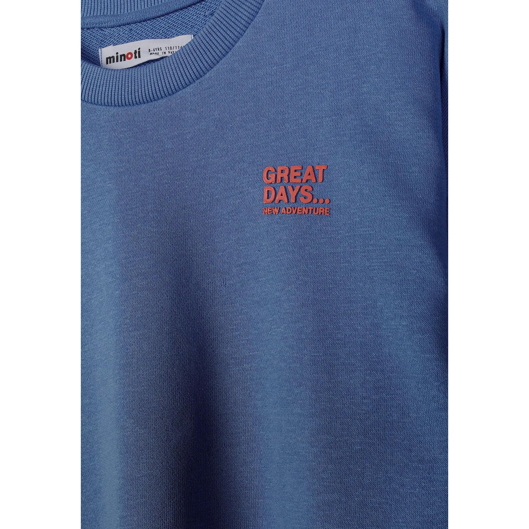 Close-up detail of blue sweatshirt showing Minoti brand label and red 'GREAT DAYS... NEW ADVENTURES' chest print on cotton fabric