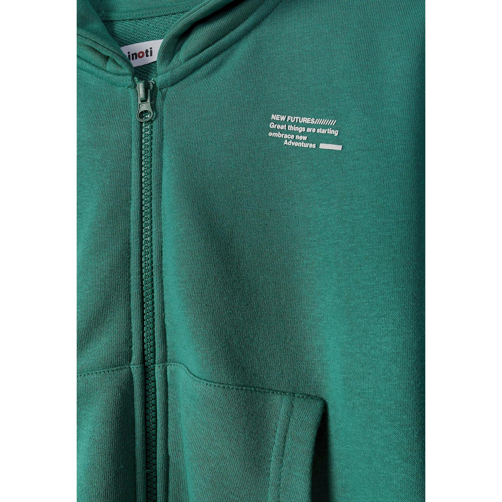 Close-up detail of green hoodie showing zip, Minoti label and text print on chest