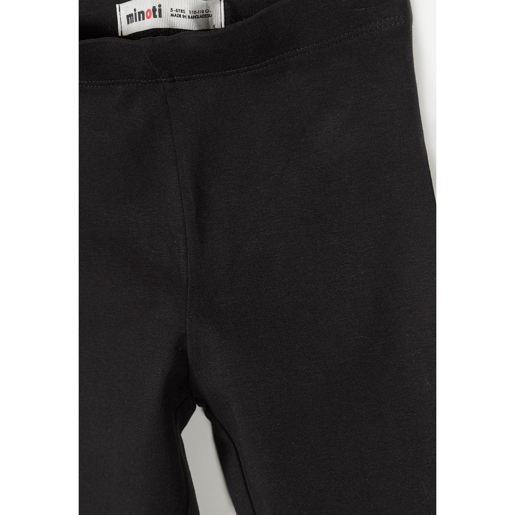 Close-up detail of black leggings showing Minoti label at waistband and cotton fabric texture