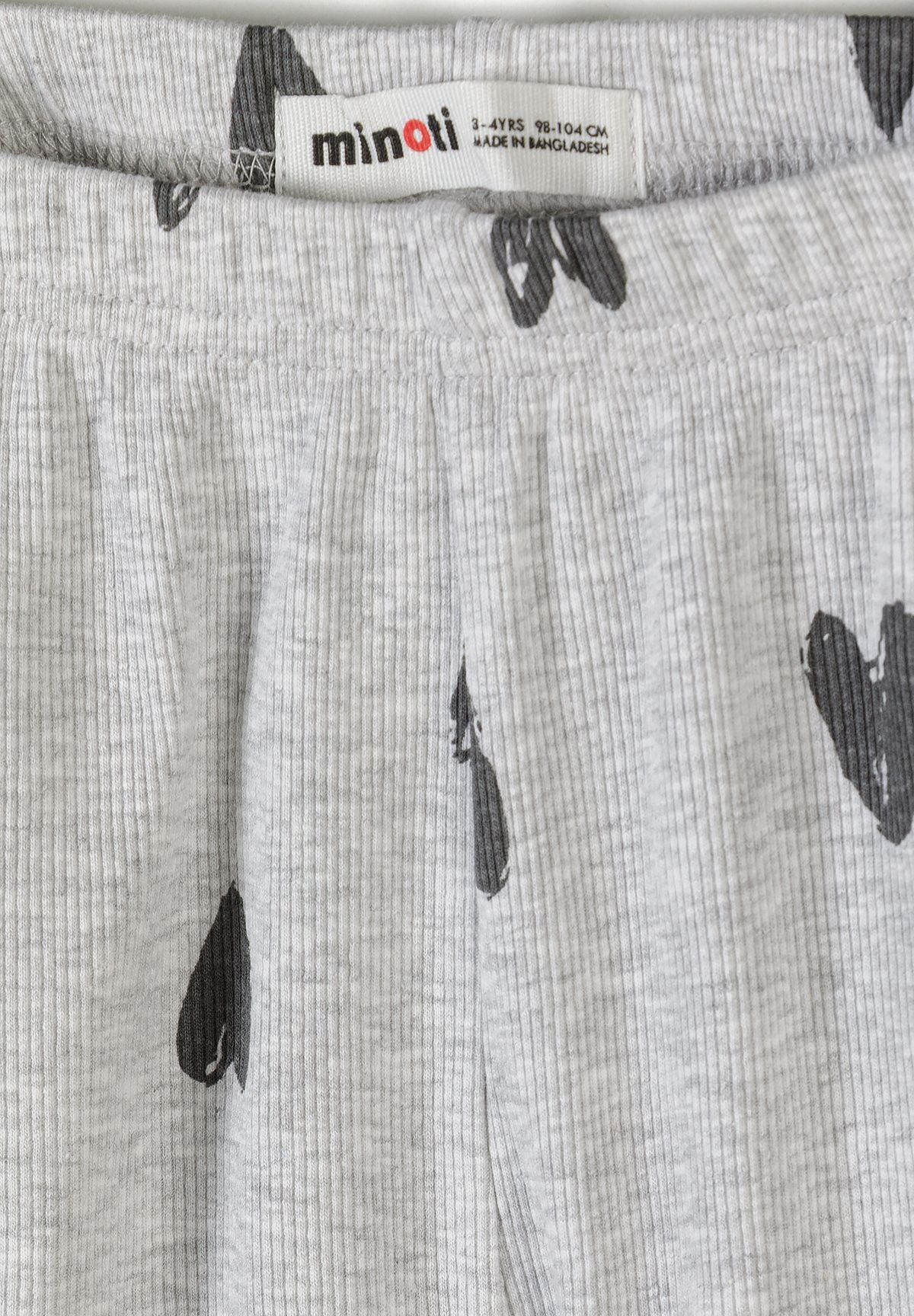 Close-up detail of cream ribbed fabric texture showing hand-drawn black hearts print pattern and crew neckline