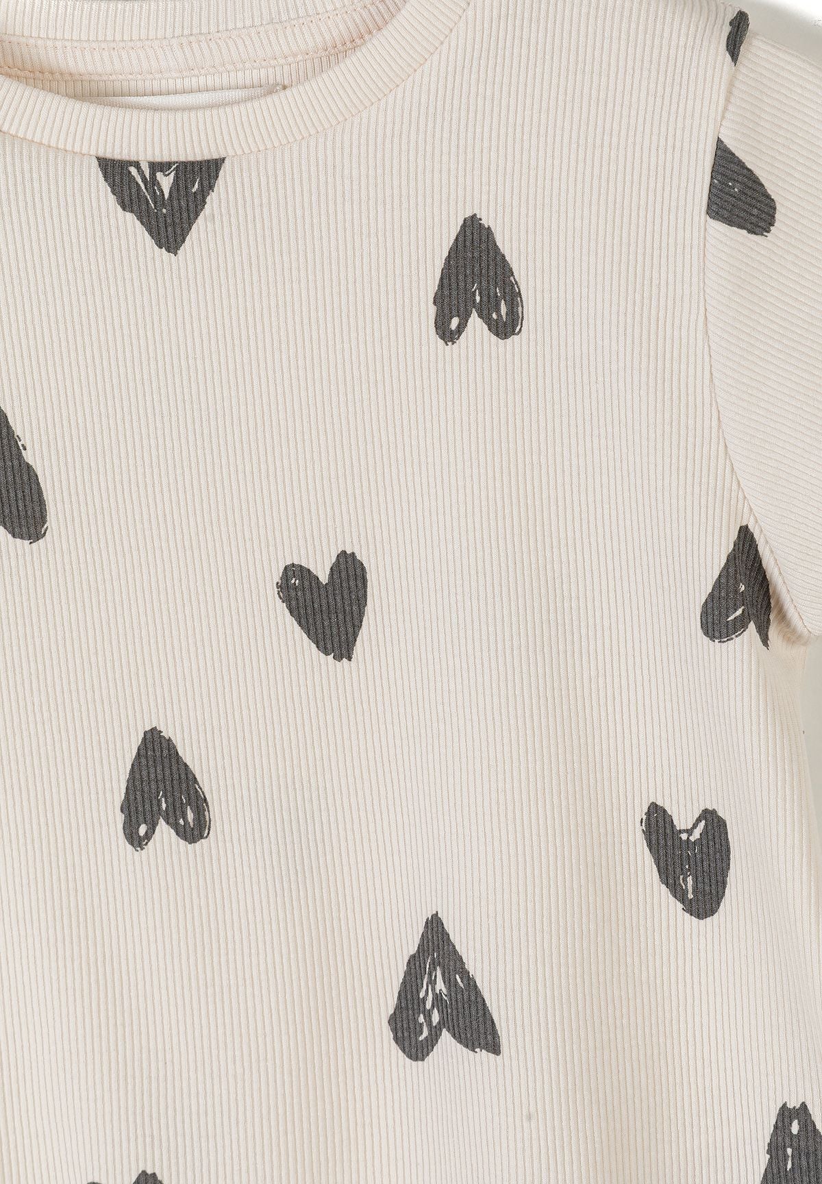 Close-up detail of cream ribbed fabric texture showing hand-drawn black hearts print pattern and crew neckline
