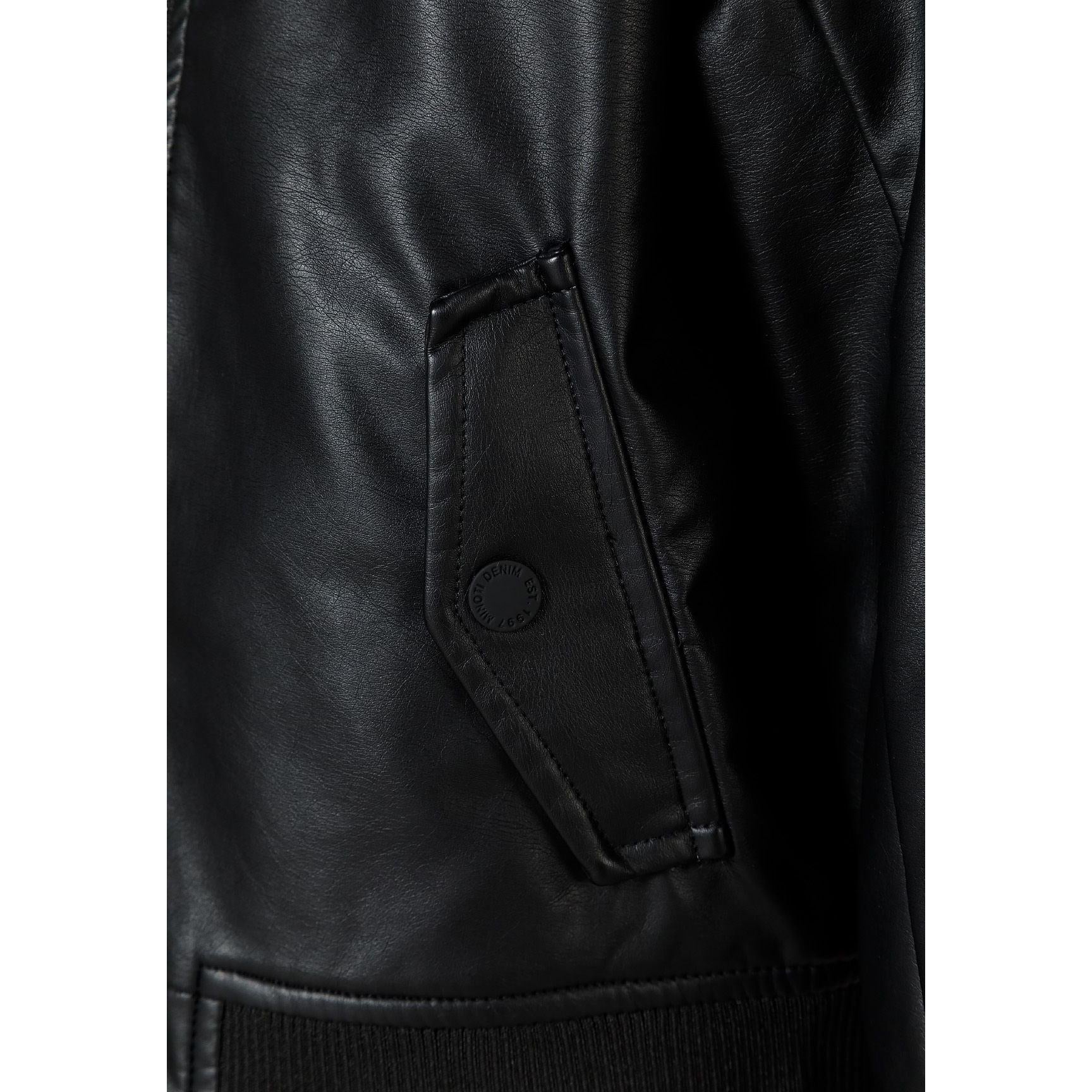 Close-up detail of black faux leather bomber jacket showing zip pocket with Minoti branded circular element on sleeve