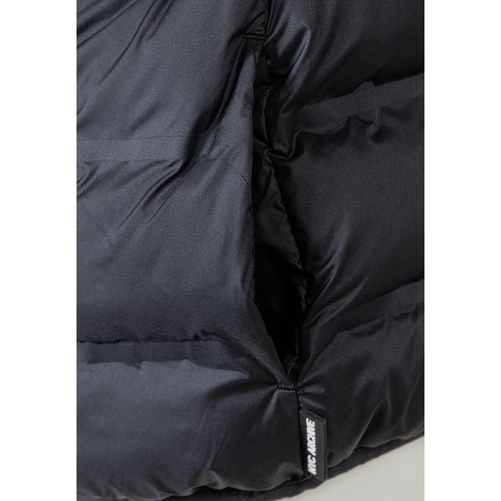 Close-up detail of black padded jacket showing quilted texture, stitching lines and fabric construction, focusing on the padded segments