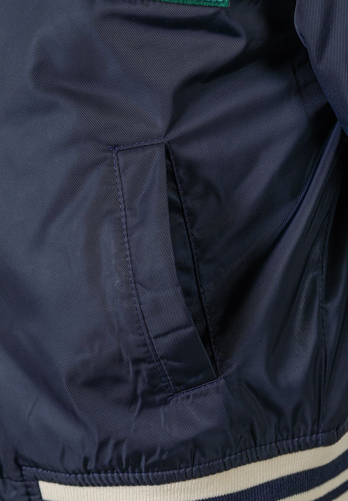 Close-up of boys navy padded varsity bomber jacket showing side pocket and ribbed hem.