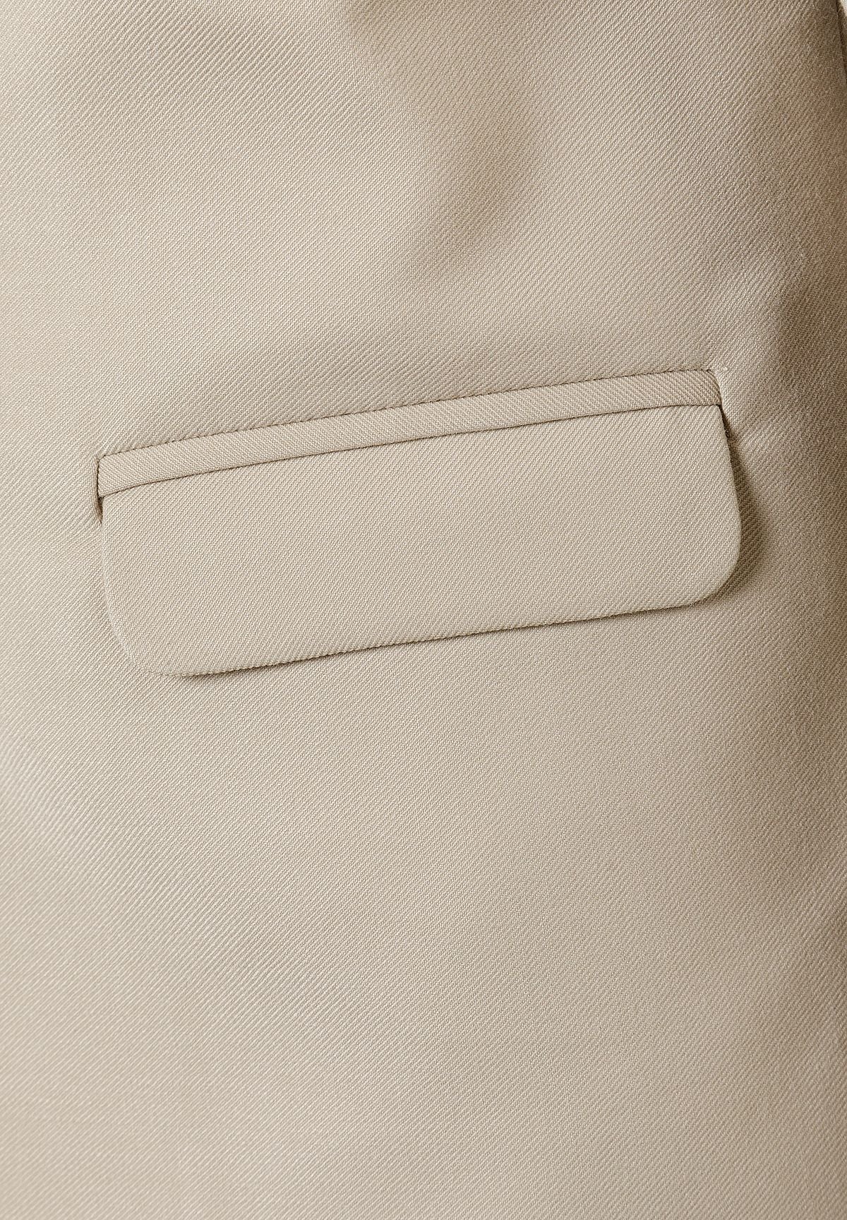 Close-up of beige blazer flap pocket and fine woven fabric.