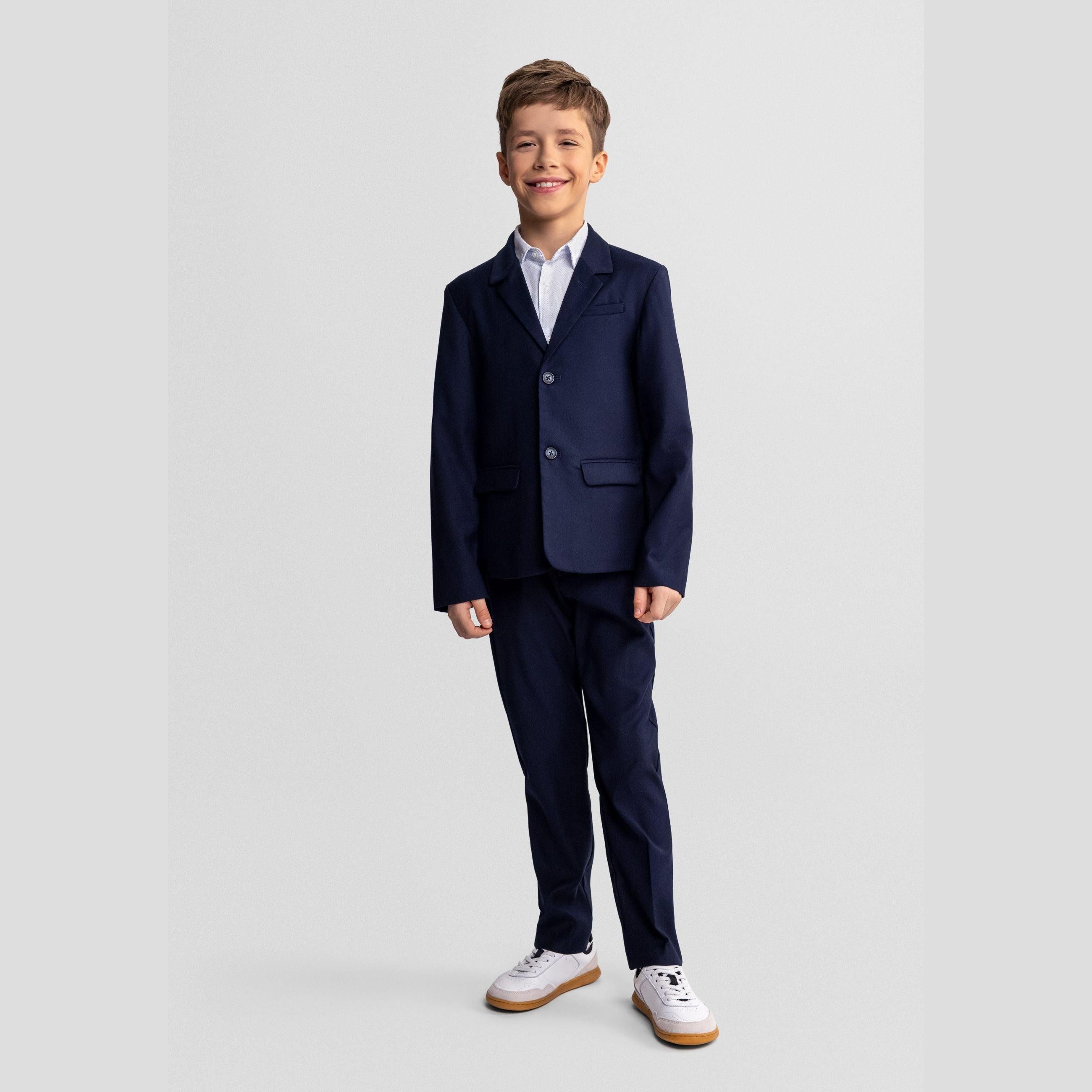 Boy wearing navy formal blazer with white shirt and matching trousers, standing confidently against grey studio background