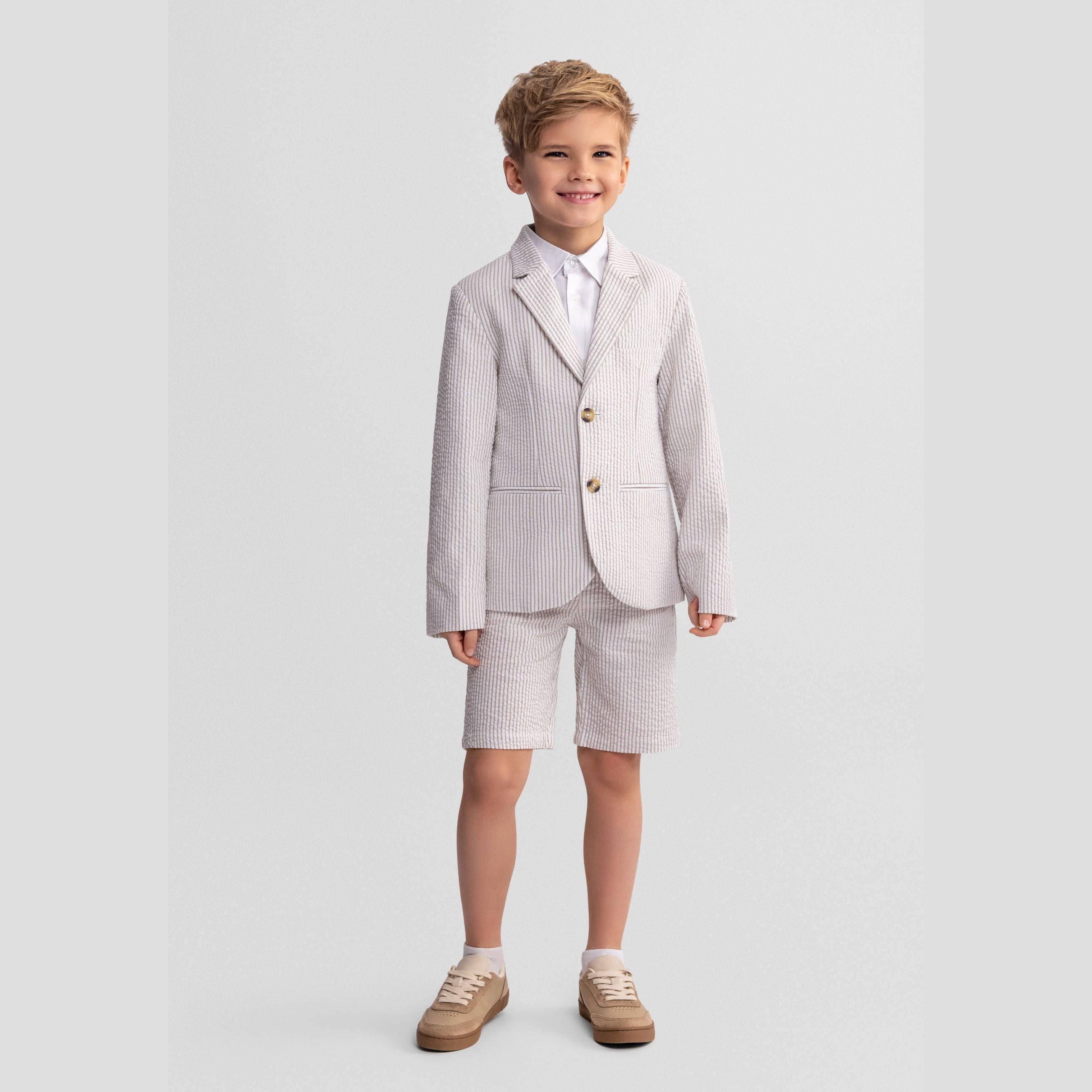 Full body shot of smiling boy in stone striped blazer with white shirt and matching shorts, standing confidently on white background