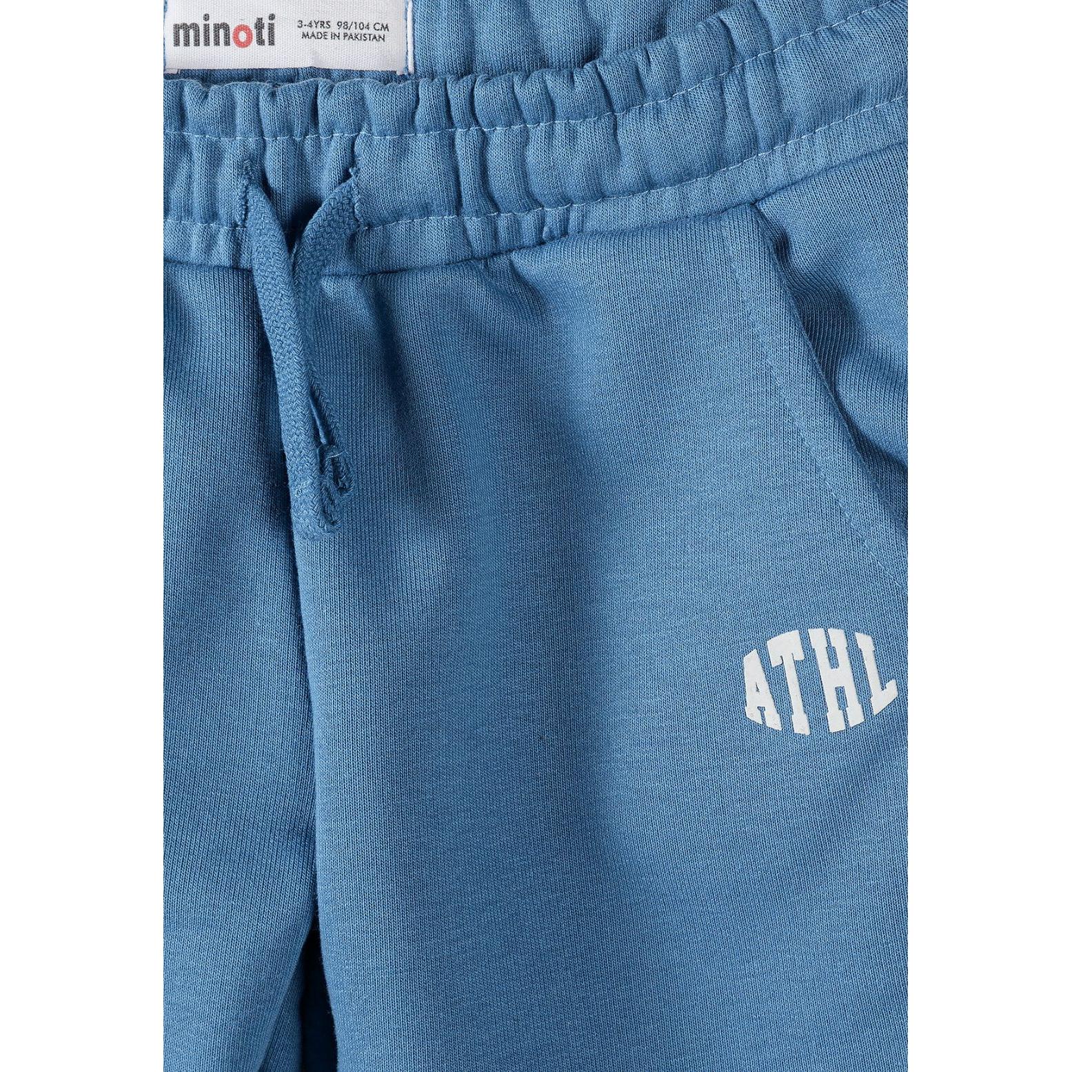 Close-up detail of blue joggers showing elastic waistband with drawstring, side pocket and white ATHL logo with Minoti brand label