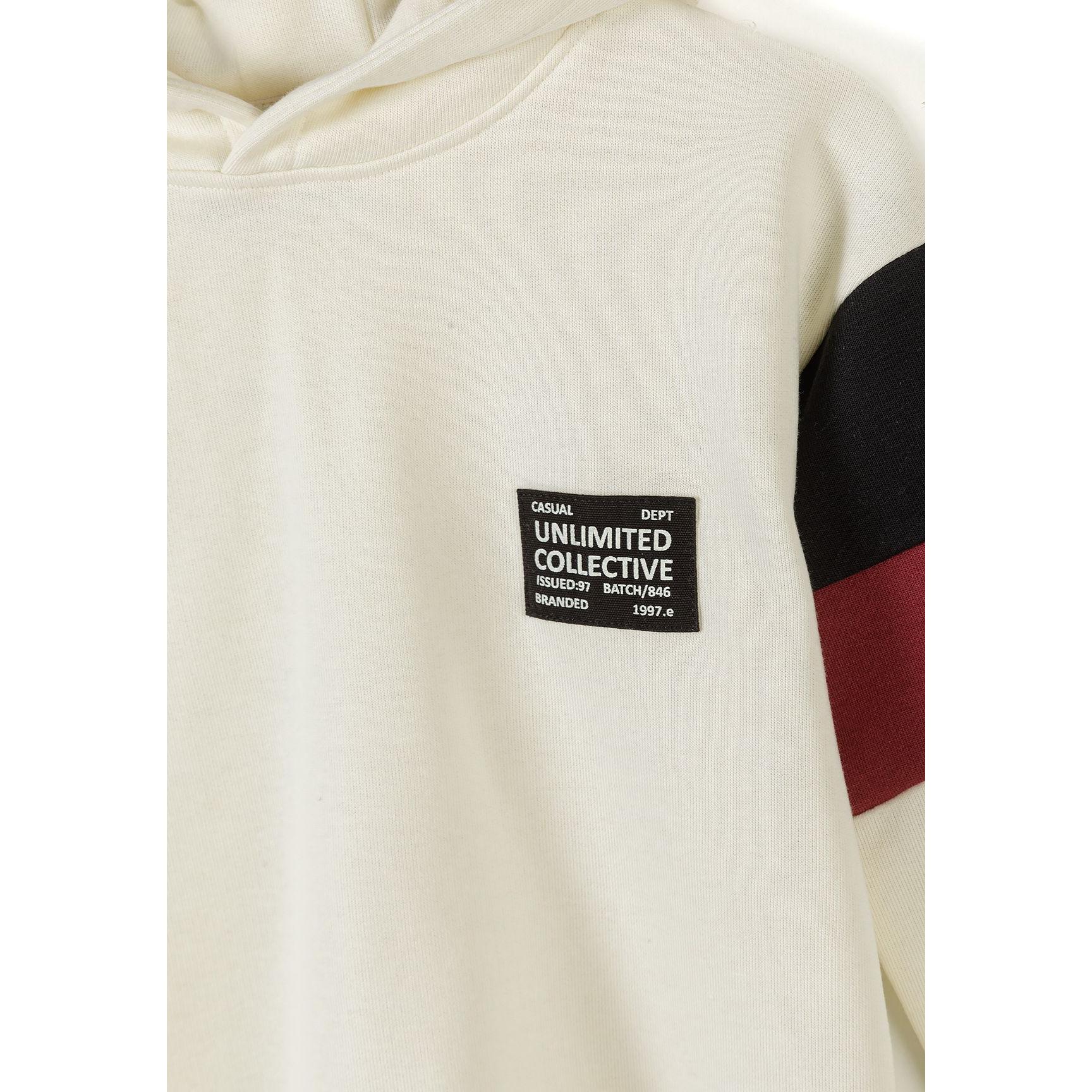 Detail shot of cream hooded sweatshirt showing black branded patch reading 'Unlimited Collective' and black contrast panel on sleeve