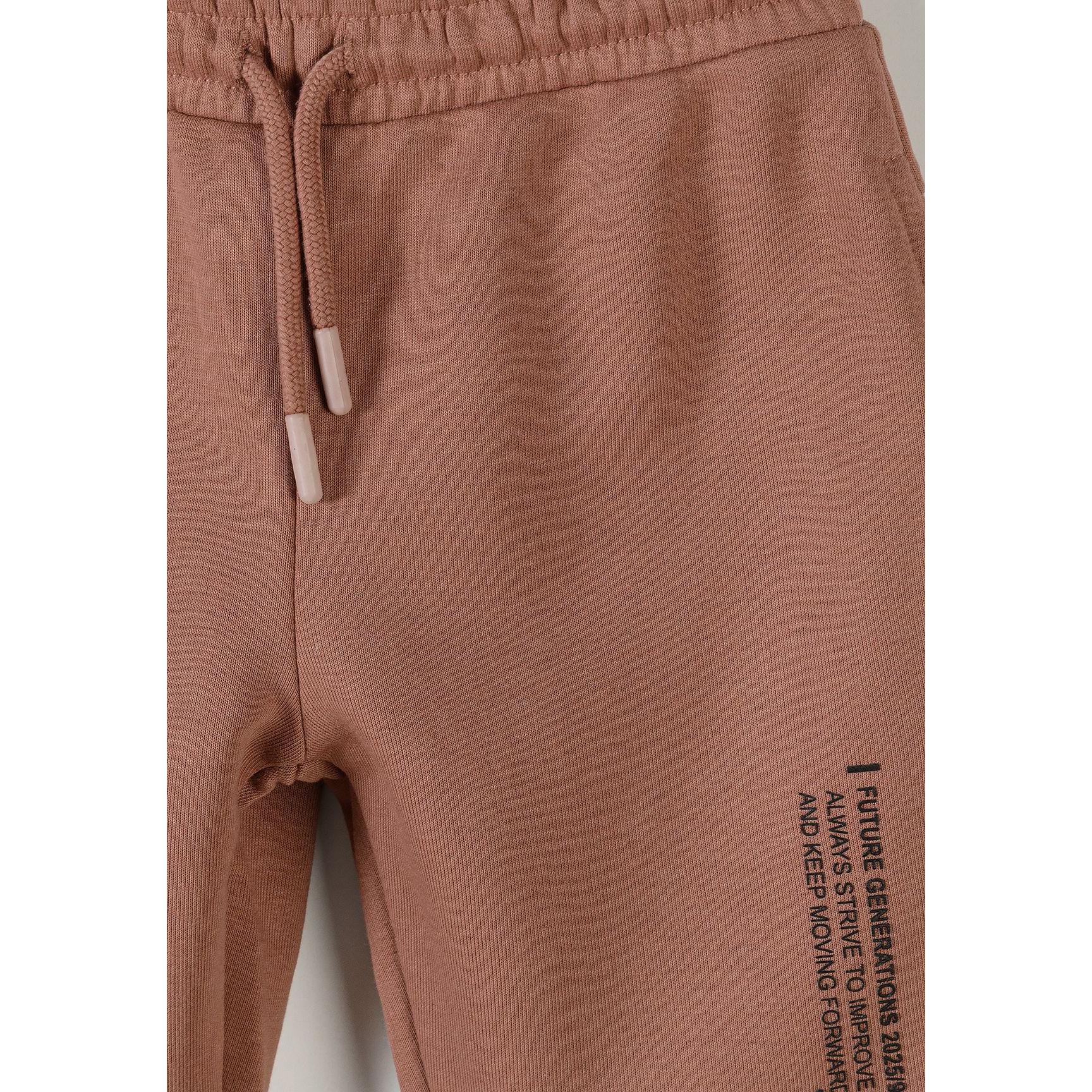Close-up detail of cognac joggers showing drawstring waistband and vertical text print on thigh area