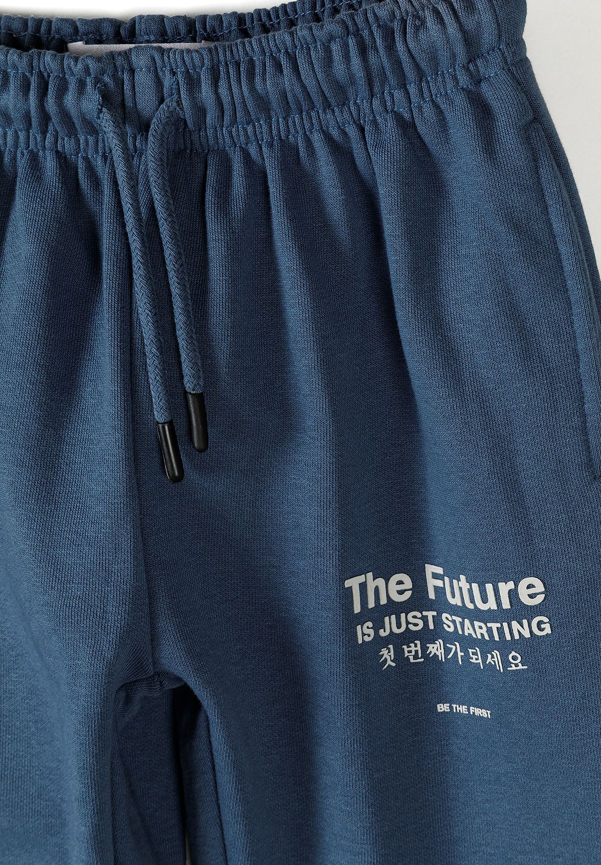 Close-up of blue jogger drawcord and white THE FUTURE IS JUST STARTING thigh print.