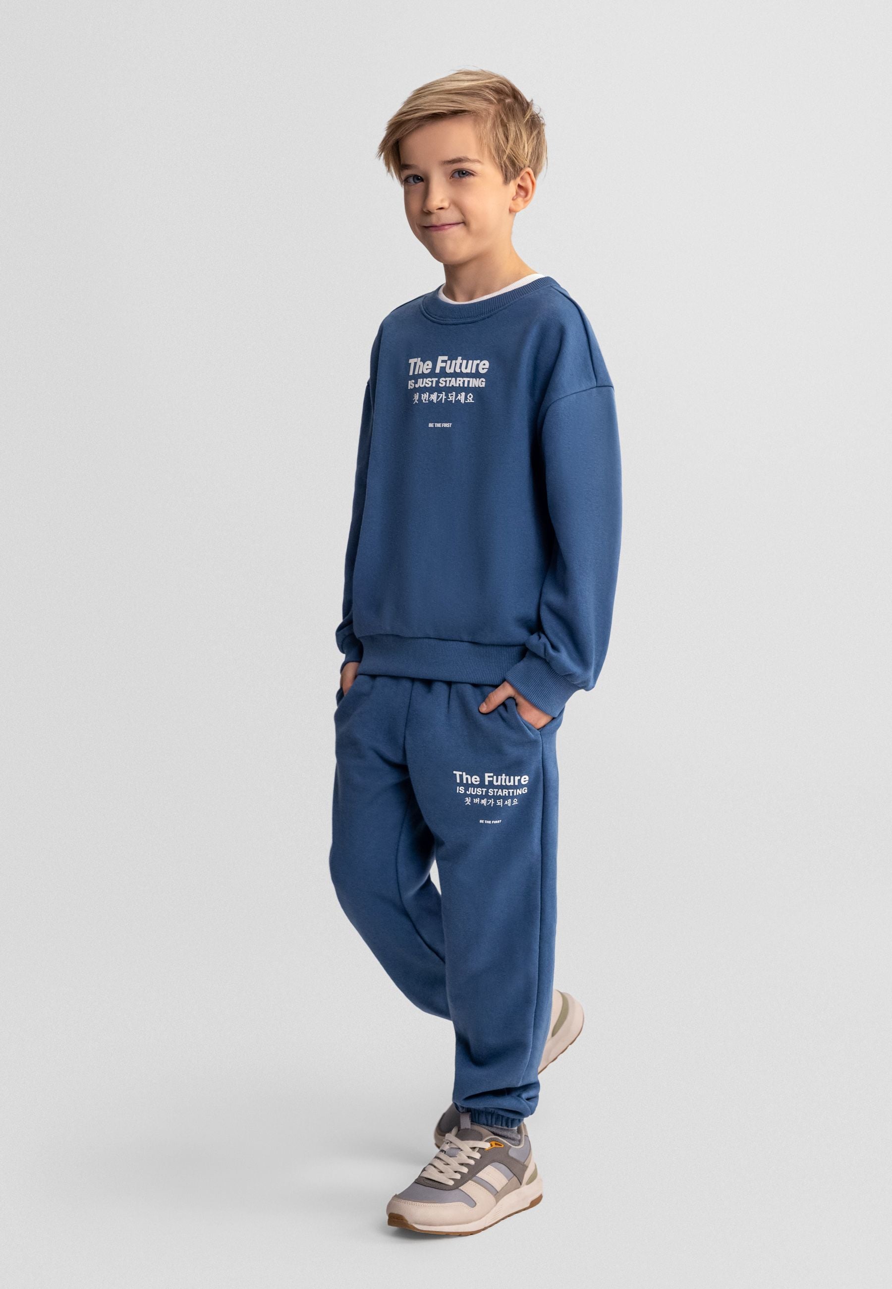 Boys blue two-piece tracksuit, front view, featuring a zip-up sweatshirt and matching trousers with pockets.