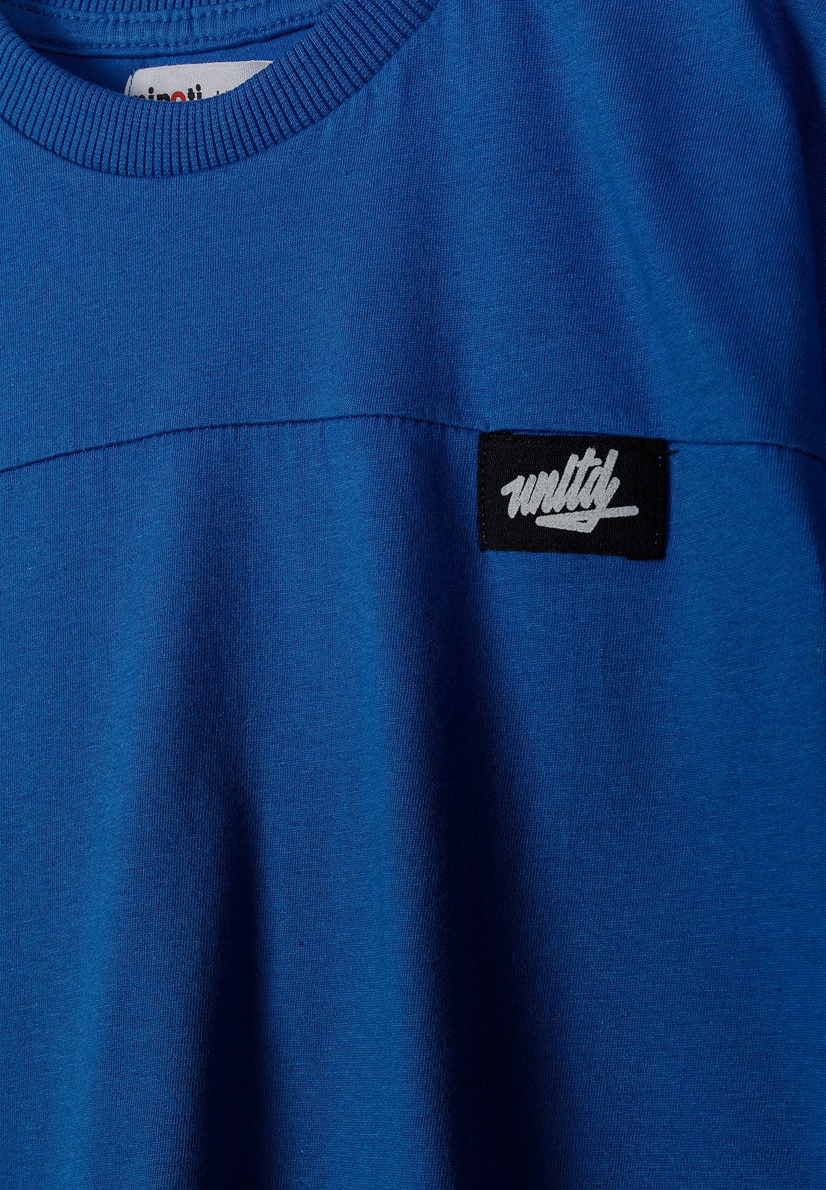 Detail of a royal blue t-shirt with a round neck and logo badge.