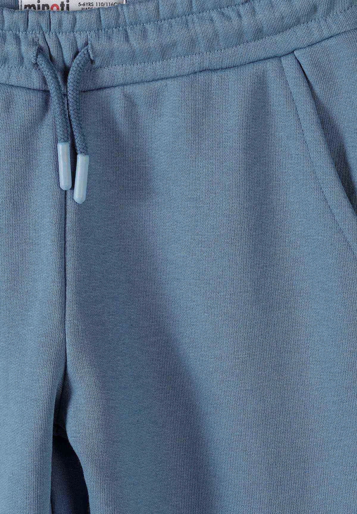 Close-up of dusty blue joggers' drawcord with pale tips beside a slanted hip pocket.