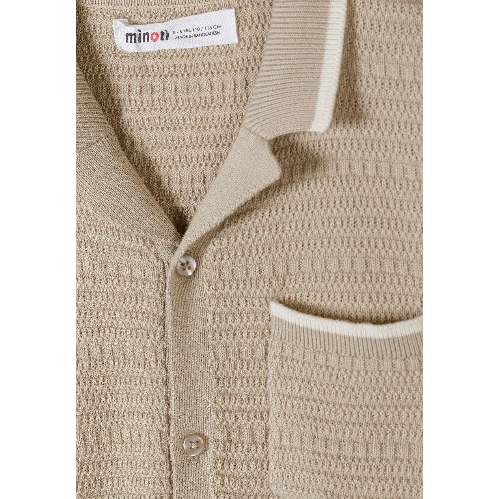 Close-up detail of beige polo shirt showing Minoti label, button placket, chest pocket and herringbone knit texture