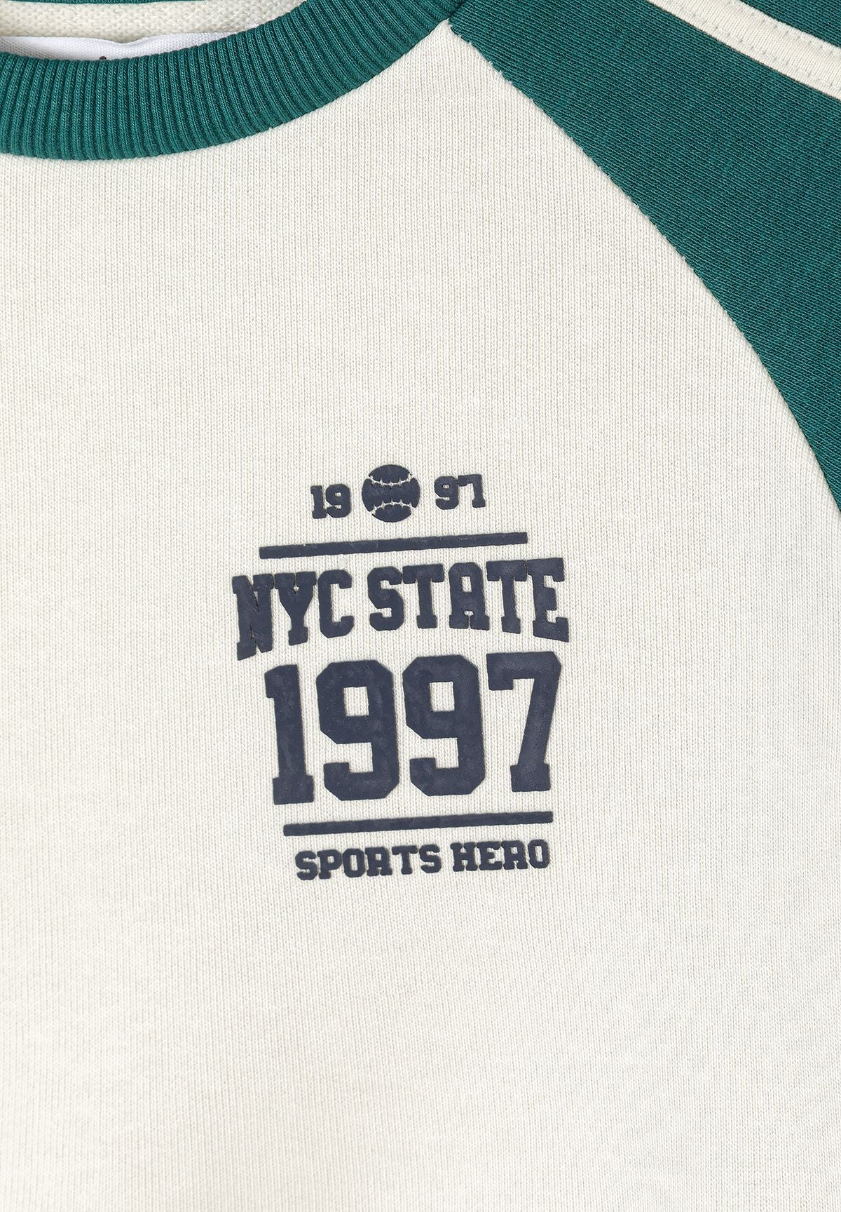 Close-up of cream sweatshirt's NYC State 1997 print and green raglan sleeve.
