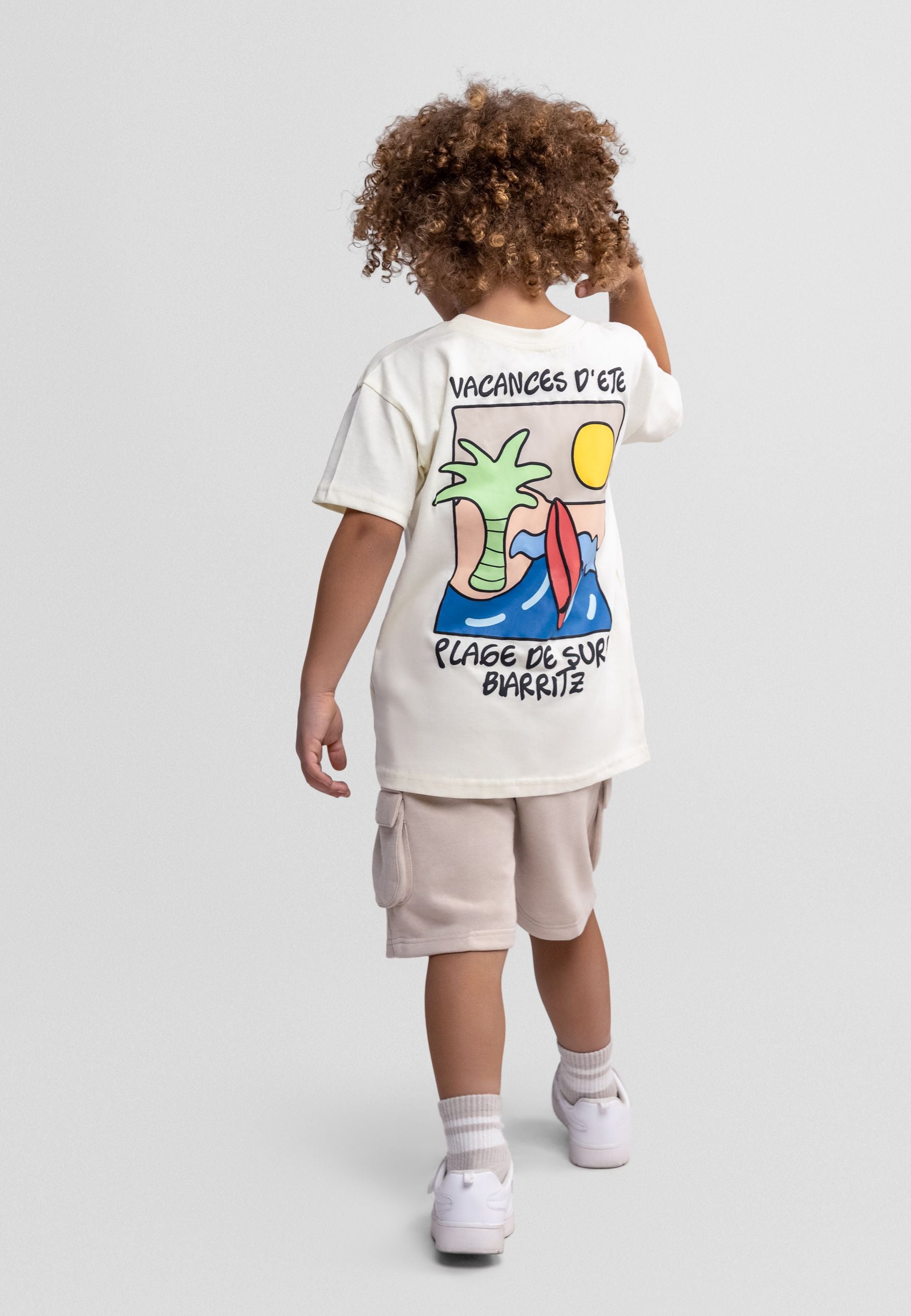 Flat lay of cream t-shirt and beige cargo shorts set showing surf beach design with palm tree and surfboard graphic