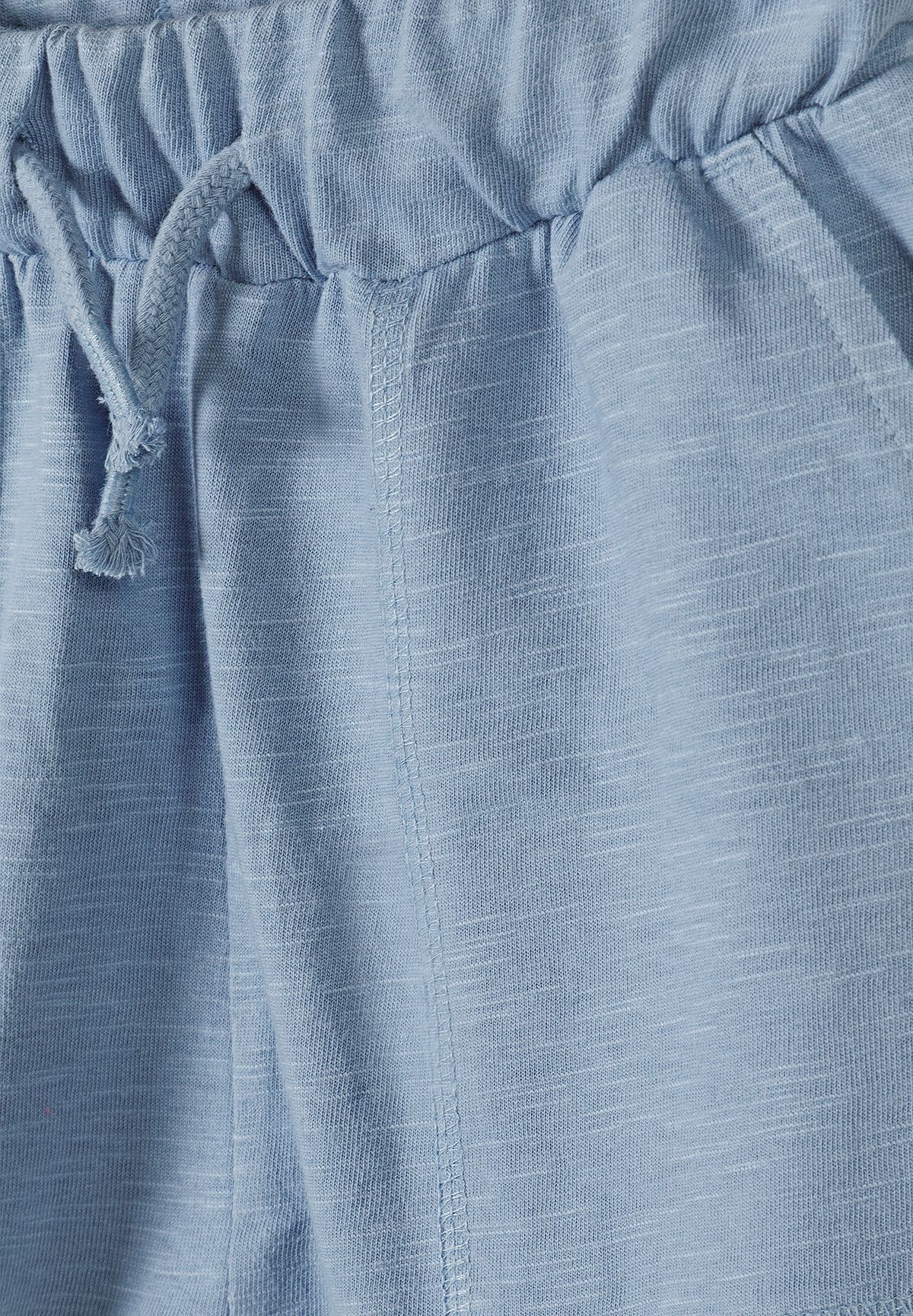 Close-up of light blue boys' shorts showing drawstring waist, stitched side pocket and slub jersey.