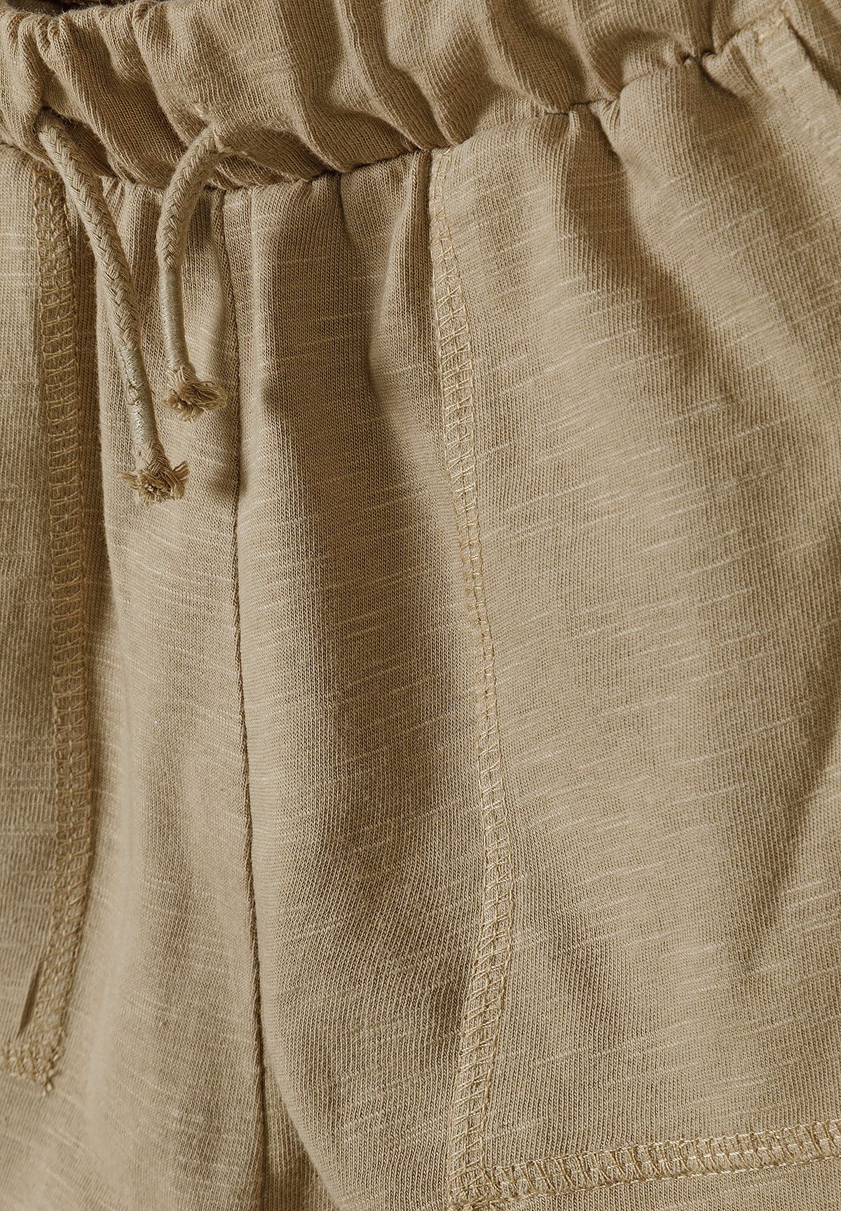 Close-up of tan jersey shorts' waist tie, gathered elastic and stitched front patch pocket.
