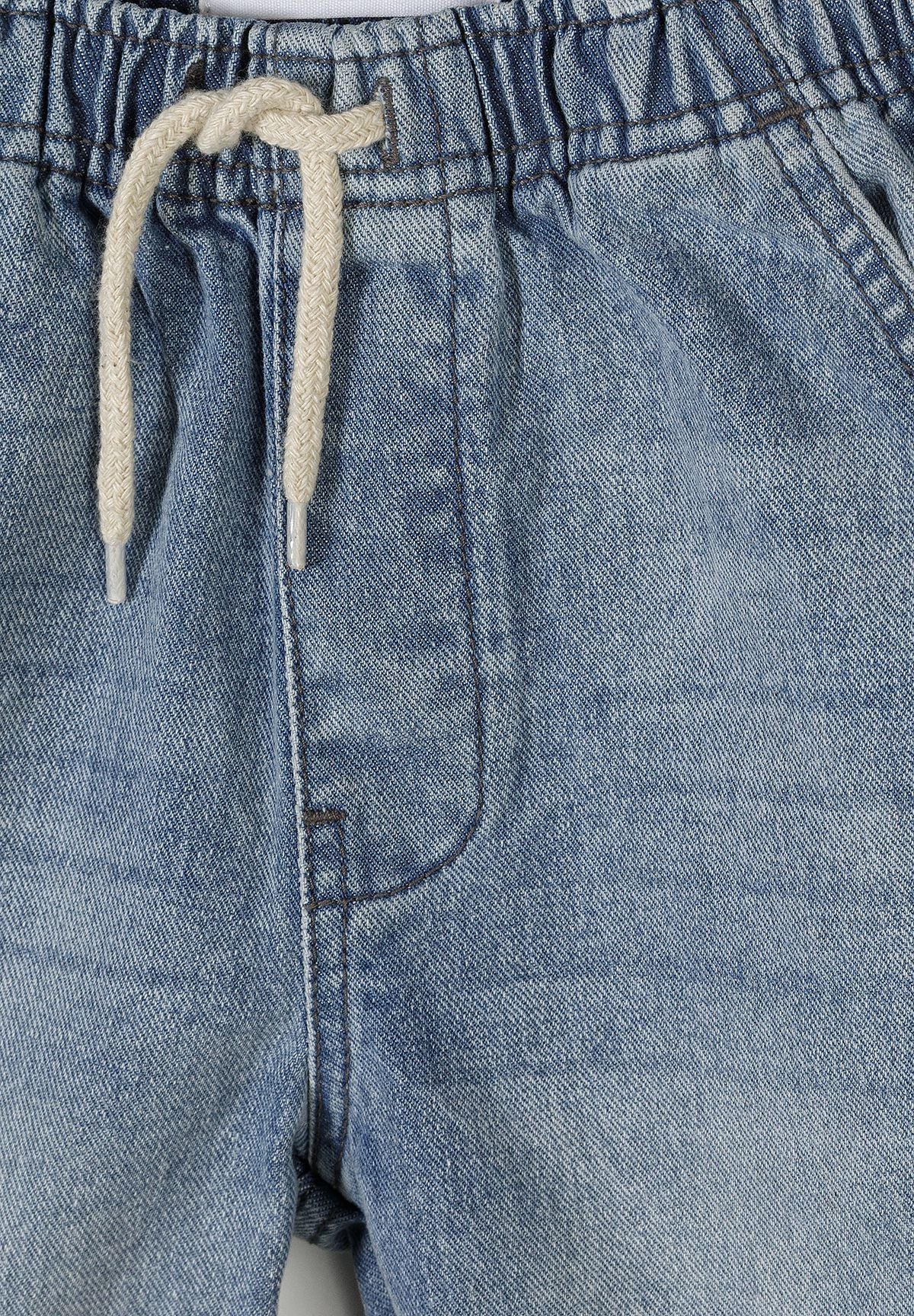 Close-up detail of denim shorts waistband showing elastic construction, cream-colored drawstring ties, and denim texture