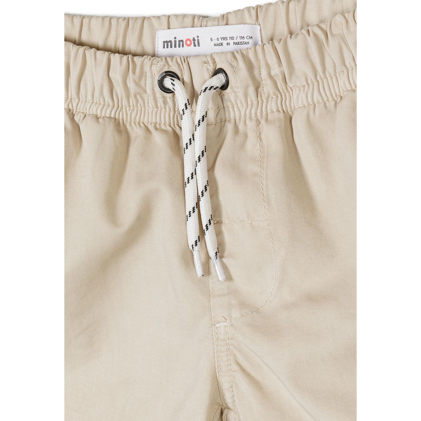 Close-up detail of beige shorts waistband showing Minoti label, elastic gathering, rope drawstring with aglets and front pocket on white background