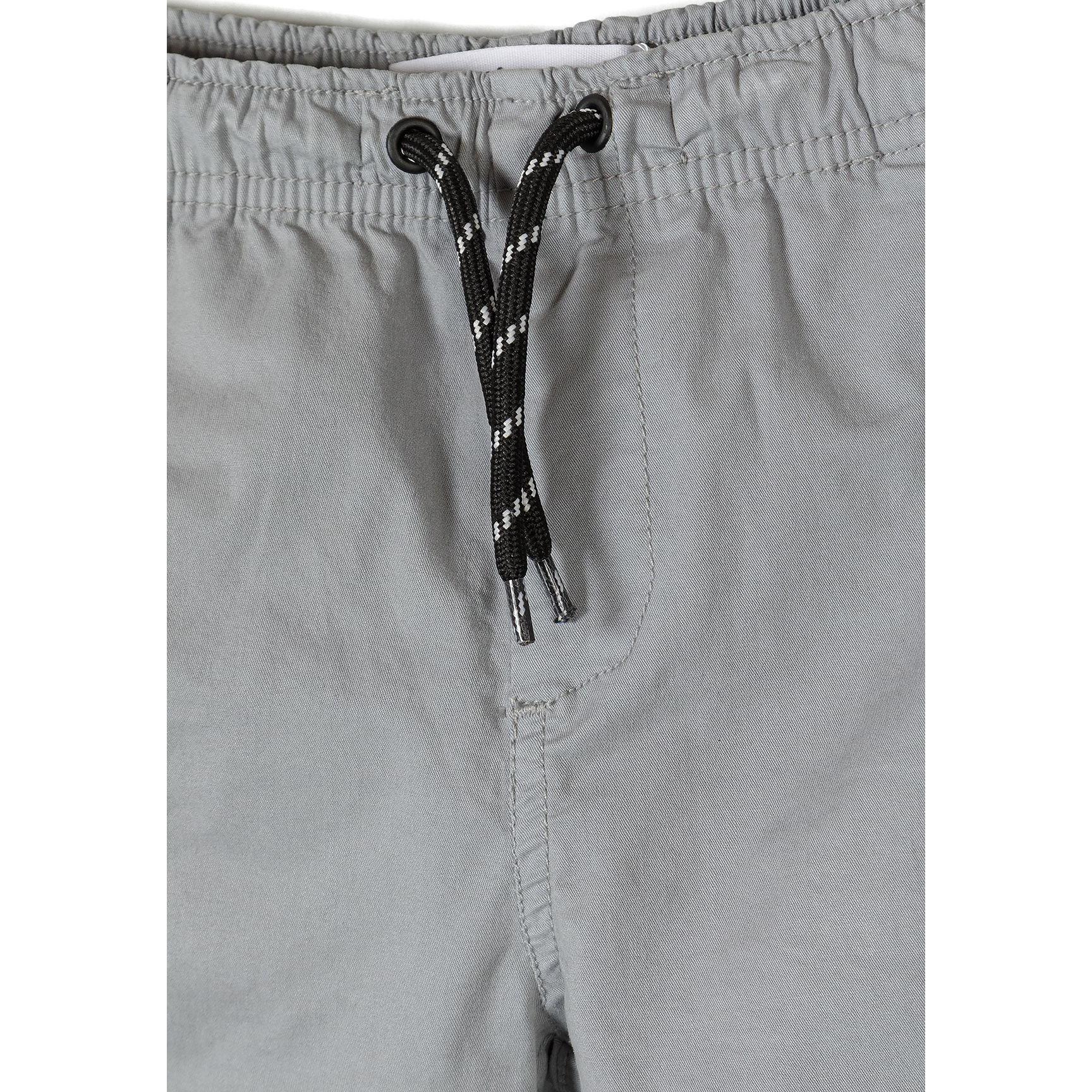 Close-up detail of grey shorts waistband showing black and white striped drawstring with metal eyelets and elastic waist construction
