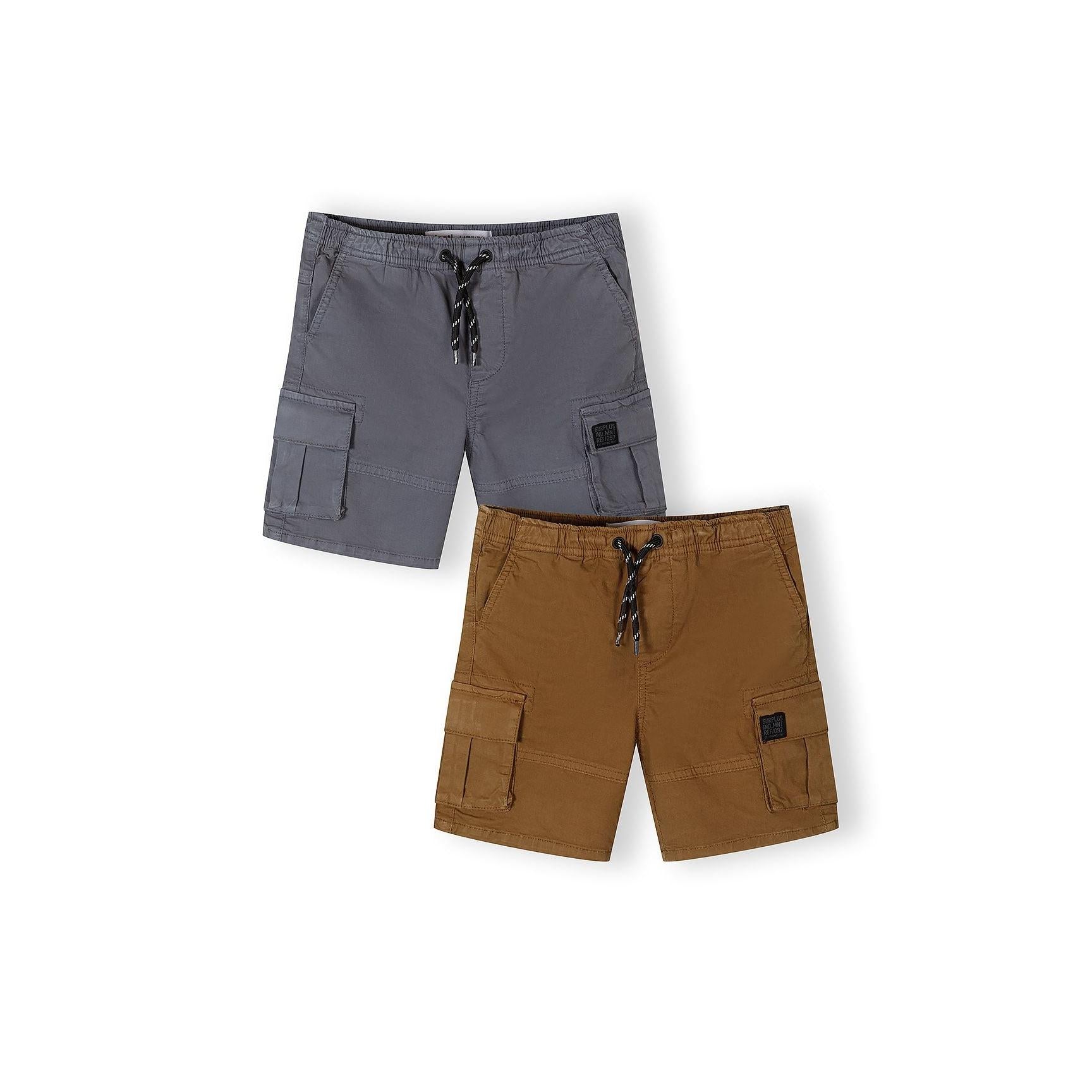 Two pairs of combat shorts laid flat - camel brown and gunmetal grey - showing cargo pockets and drawstring waists on white background